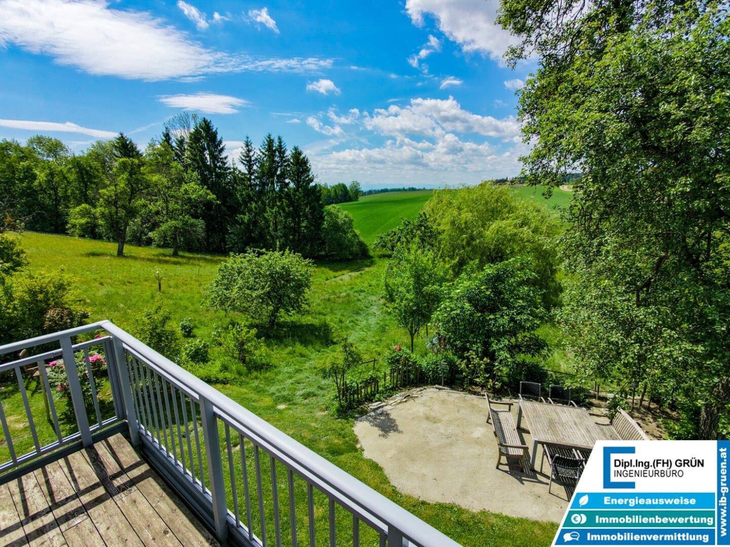 Weitläufiger Ausblick von einem Balkon über die grüne Landschaft mit Feldern und Bäumen.
