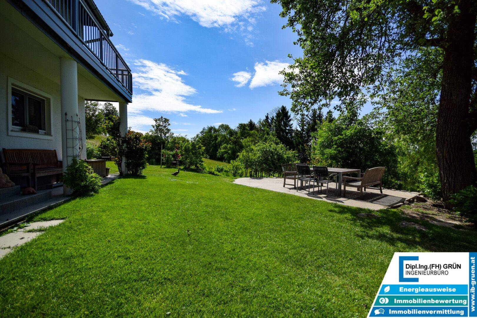 Große Rasenfläche vor dem Haus mit einer gepflasterten Terrasse und Esstisch im Freien.
