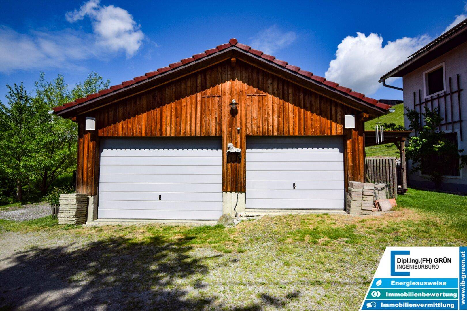 Rustikale Doppelgarage aus Holz mit zwei weißen Toren, bietet Platz für zwei Fahrzeuge.