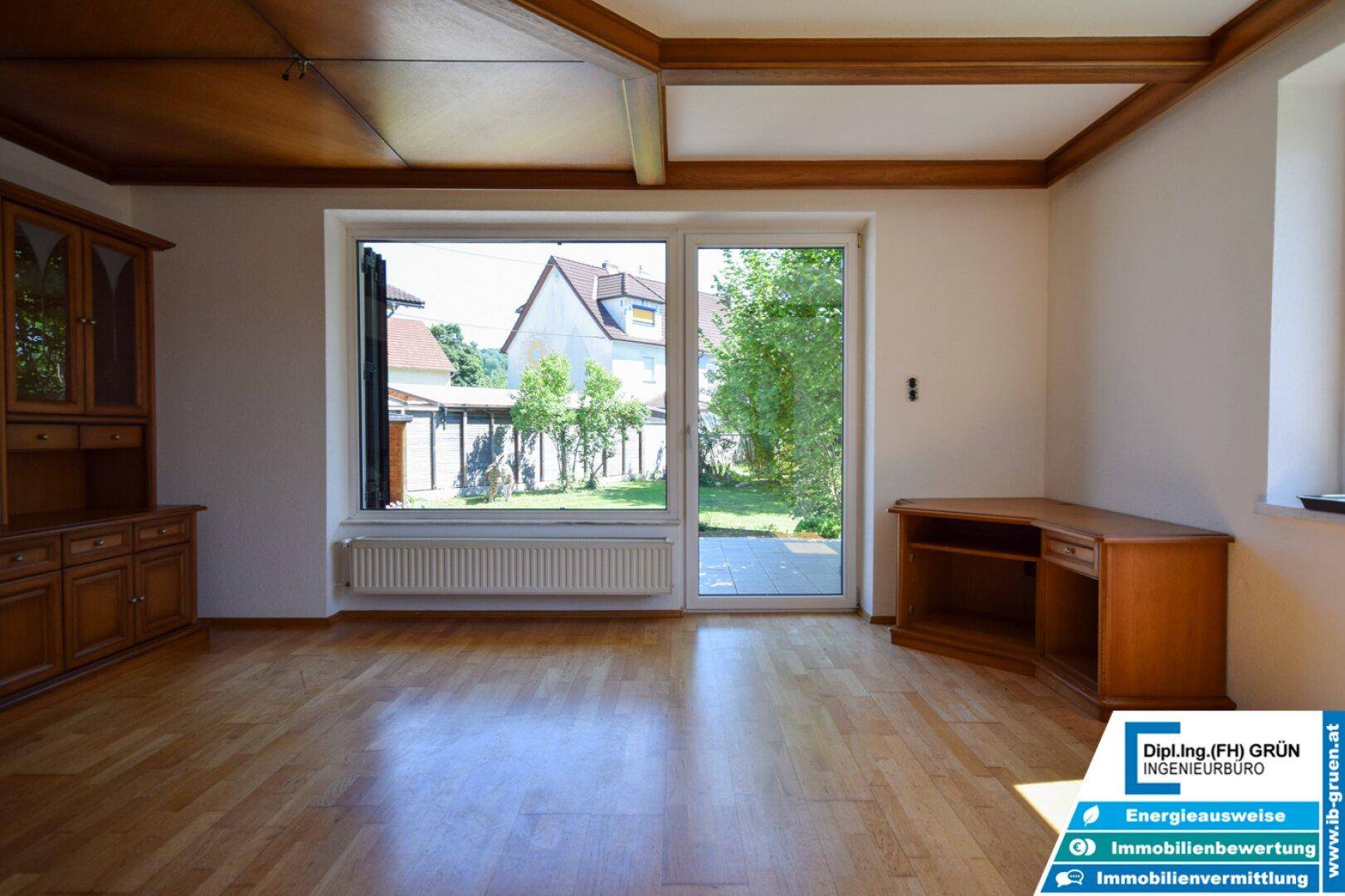 Geräumiges Wohnzimmer mit Parkettboden, Holzdecke und großem Fenster zum Garten.