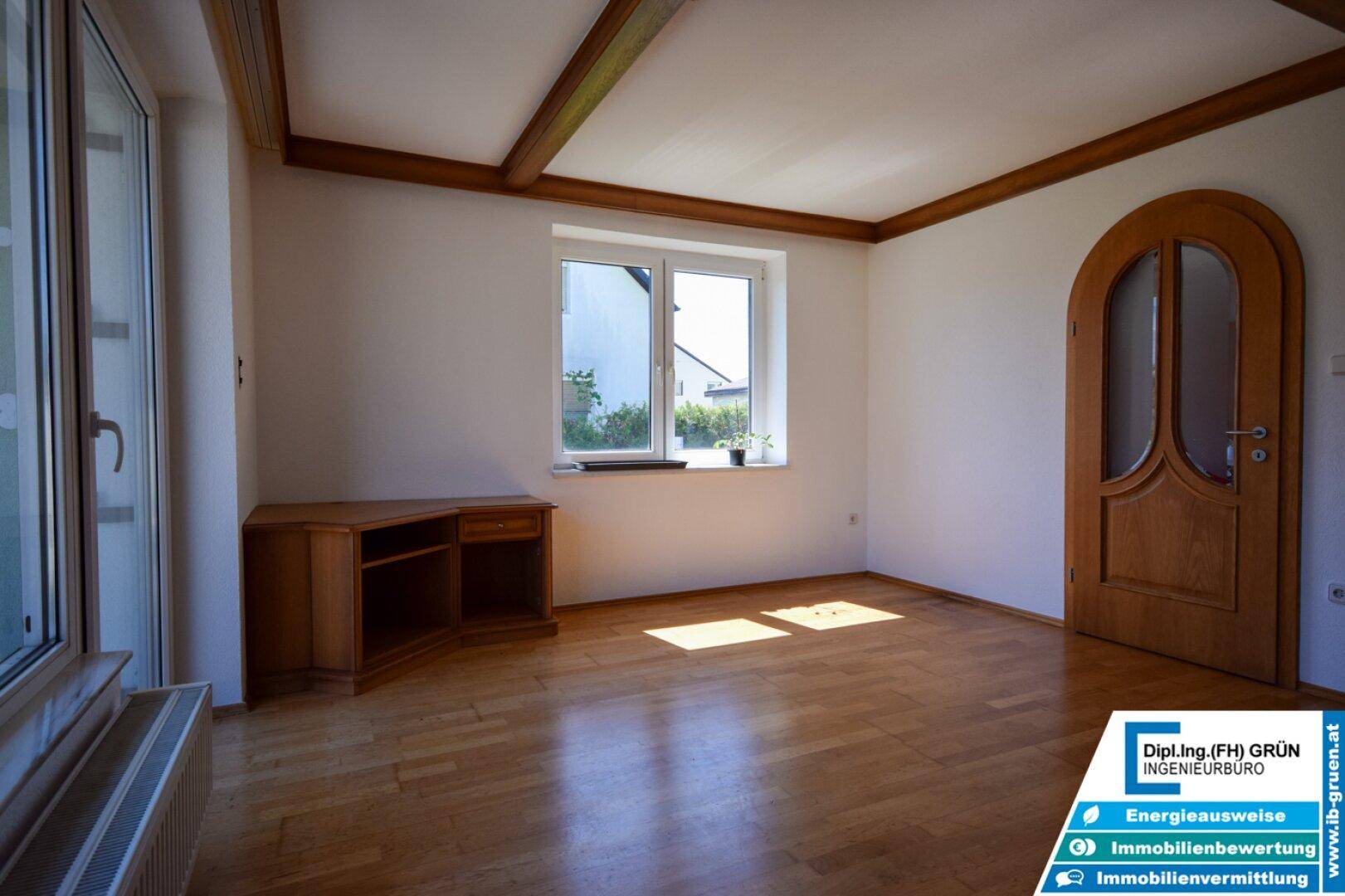 Helles Wohnzimmer mit Parkettboden, Holzdecke und Fenster mit Blick ins Grüne.