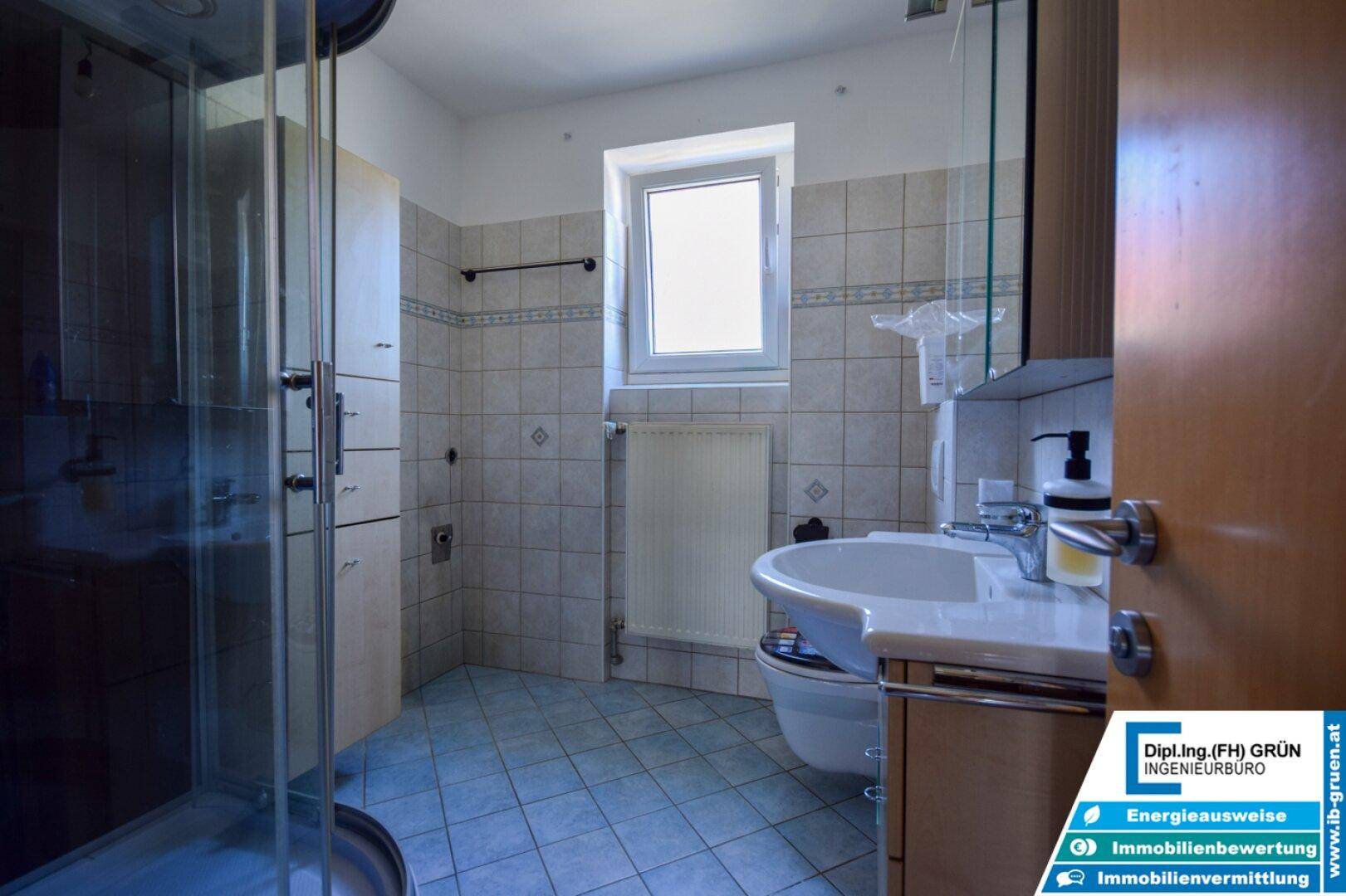 Badezimmer mit Dusche, WC, Waschbecken und Fenster.