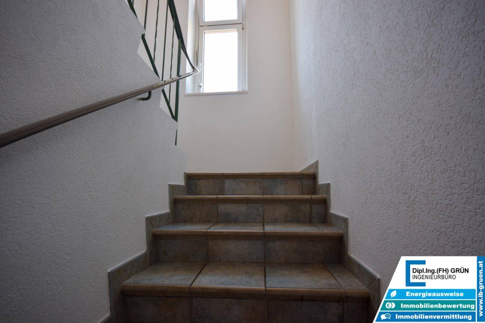 Geflieste Treppe mit Metallgeländer und Fenster, die zu den oberen Stockwerken führt.