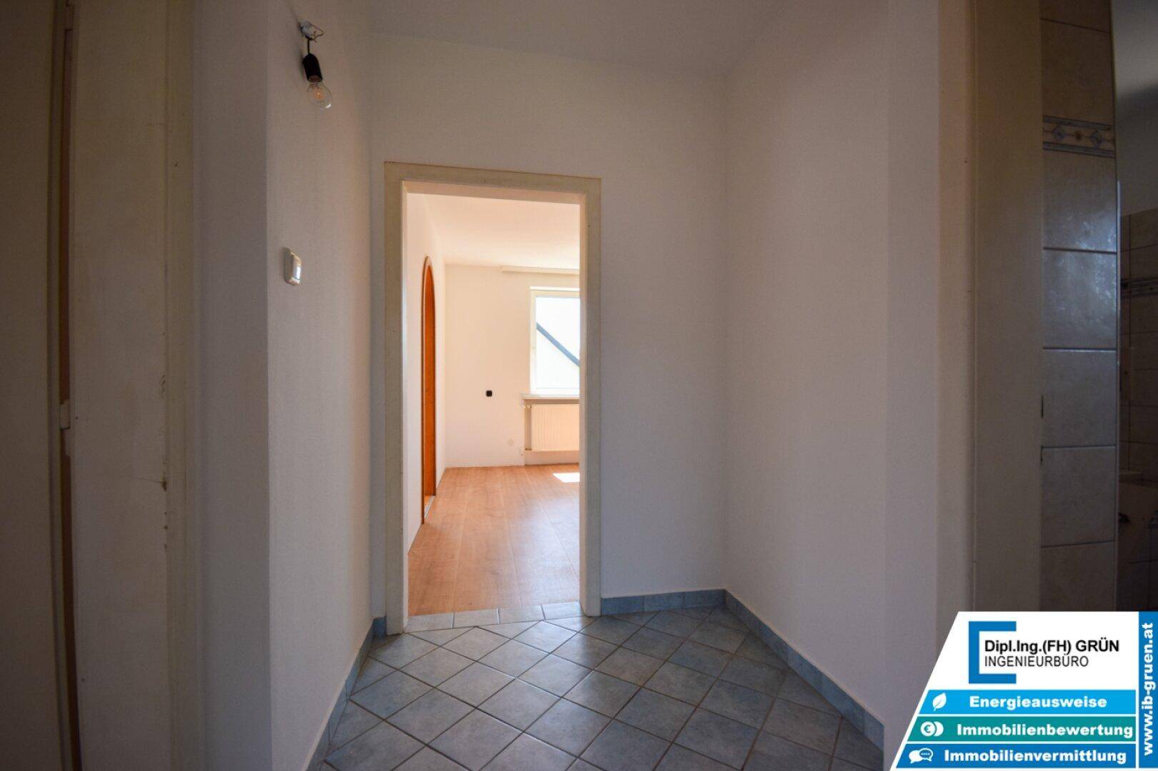 Heller Flur mit Fliesenboden und Zugang zu einem weiteren Raum mit Parkettboden.