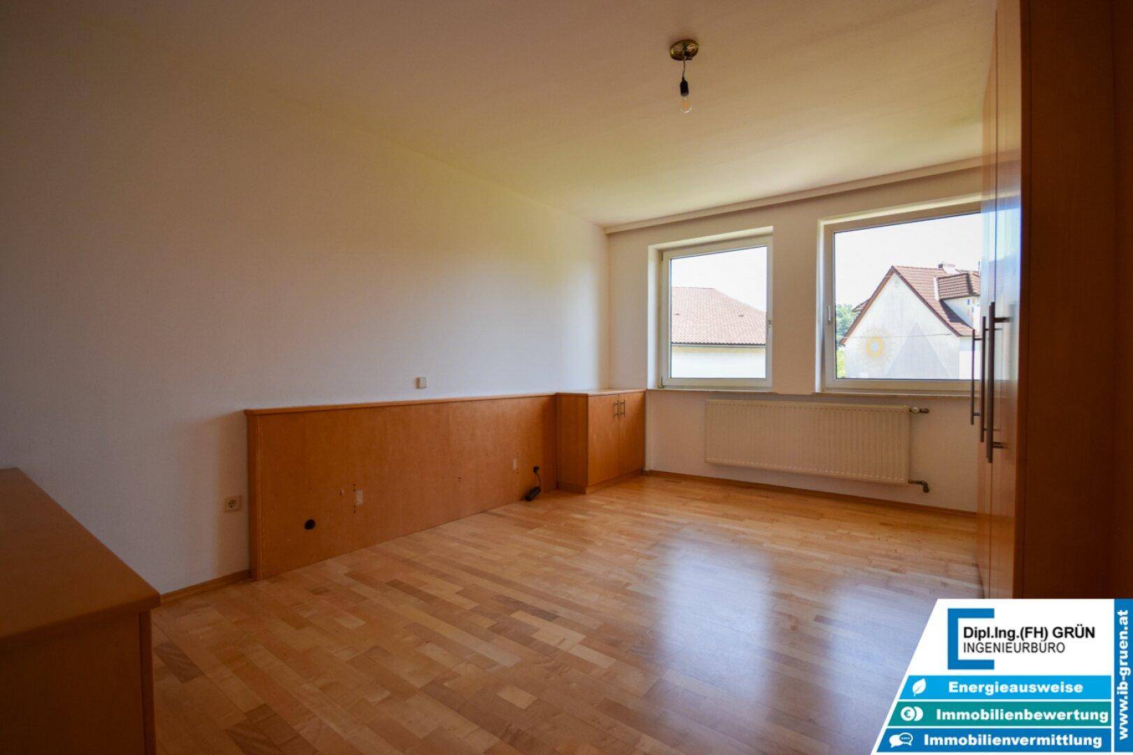 Geräumiges Schlafzimmer mit Parkettboden und zwei Fenstern, die viel Tageslicht hereinlassen.