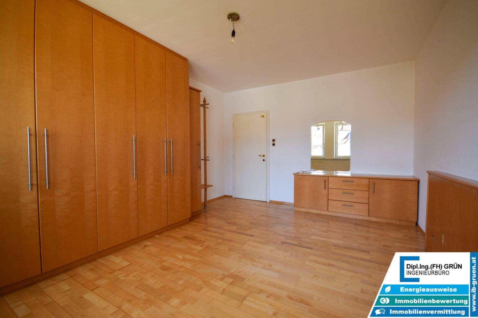 Schlafzimmer mit Parkettboden, Einbauschränken und einem Fenster, das den Raum erhellt.