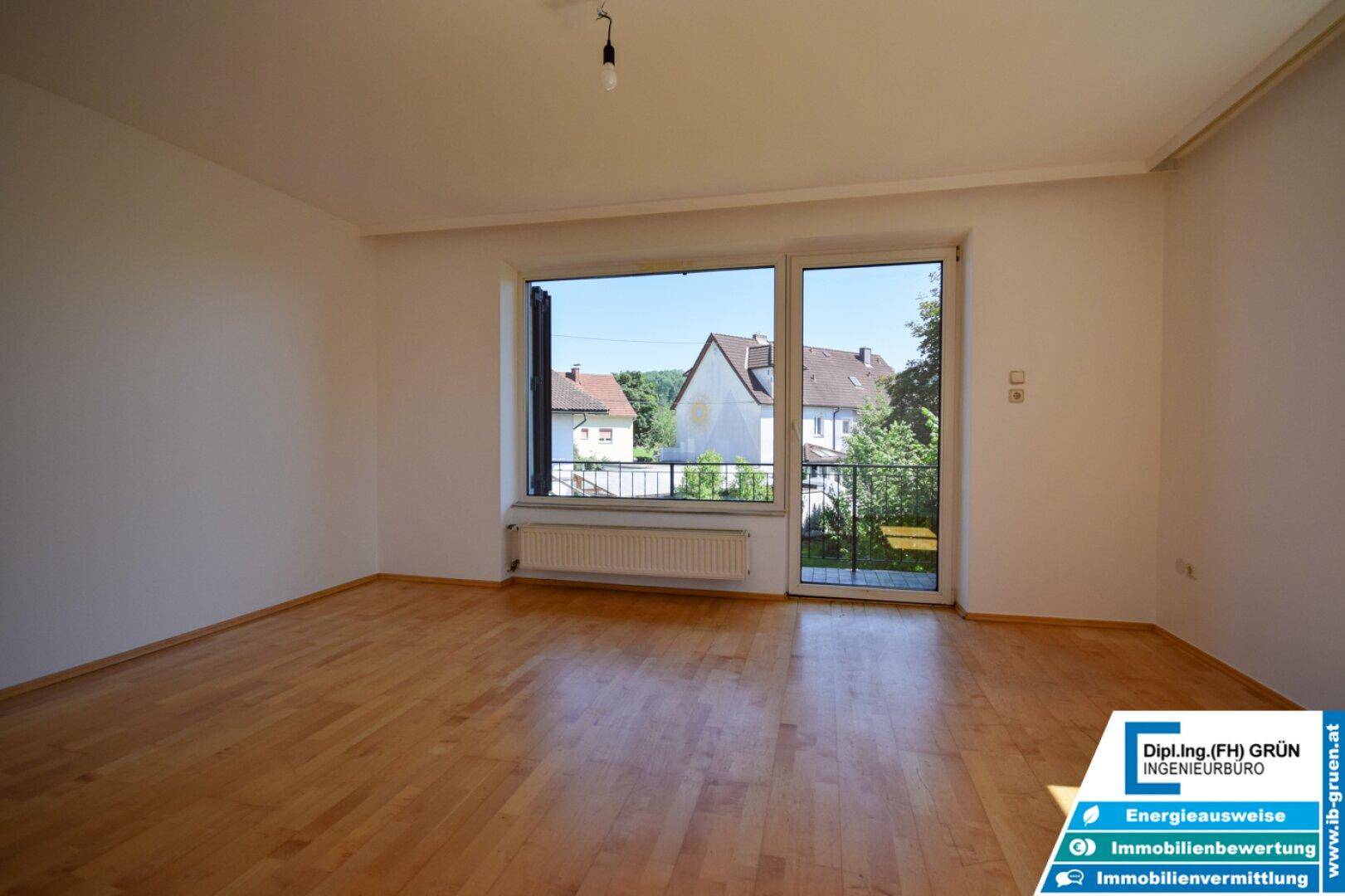 Helles Wohnzimmer mit Parkettboden und großem Fenster mit Zugang zum Balkon.