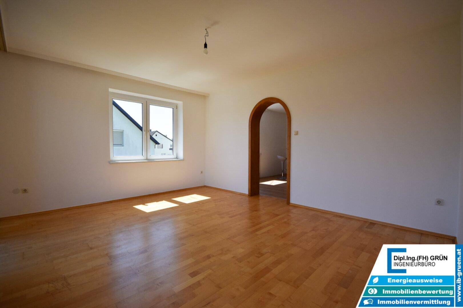 Geräumiges Wohnzimmer mit Parkettboden und einem Rundbogen, der zu einem weiteren Raum führt.