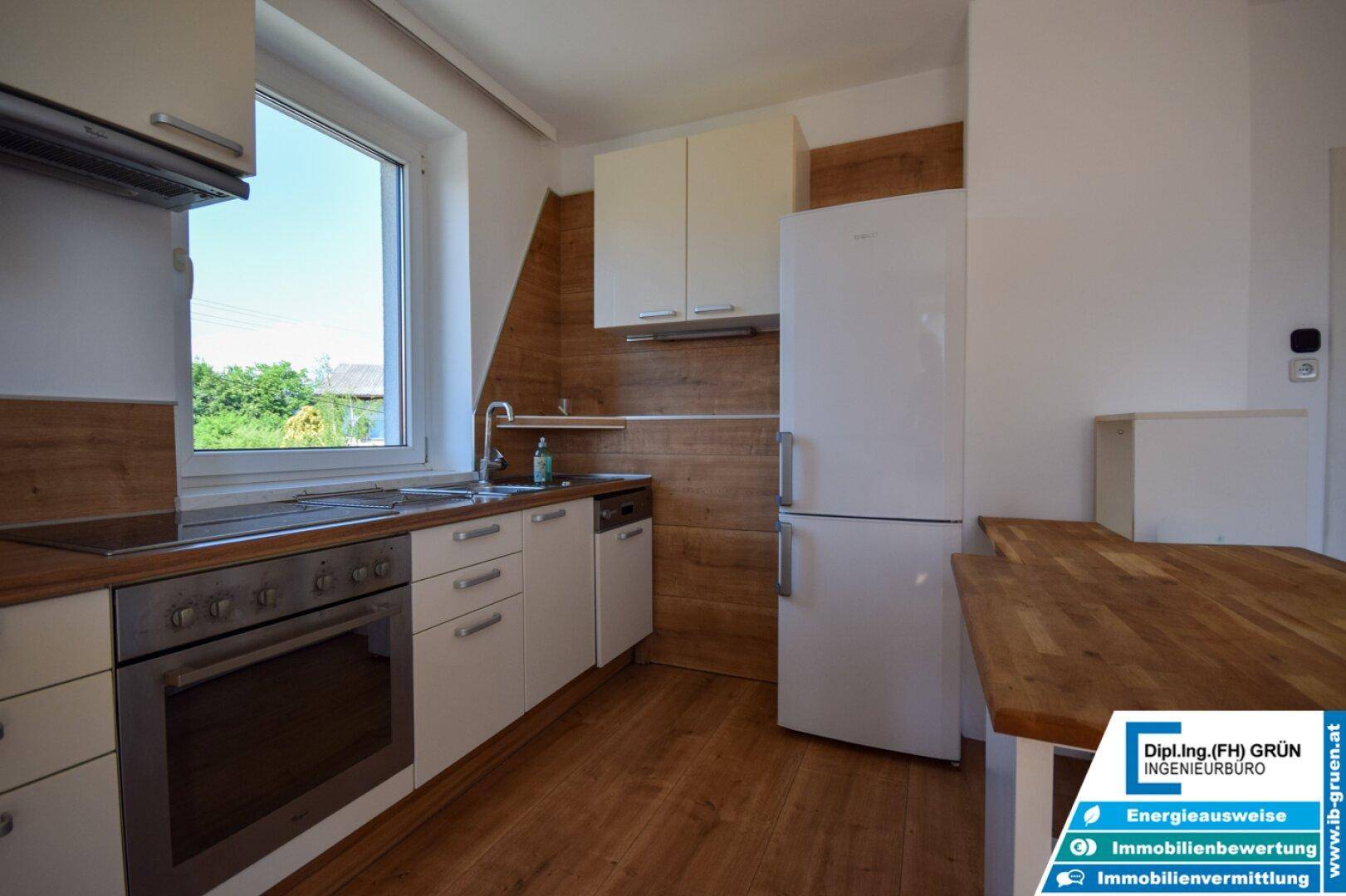 Moderne Küche mit Holzboden, Einbaugeräten und einem Fenster mit Blick ins Grüne.