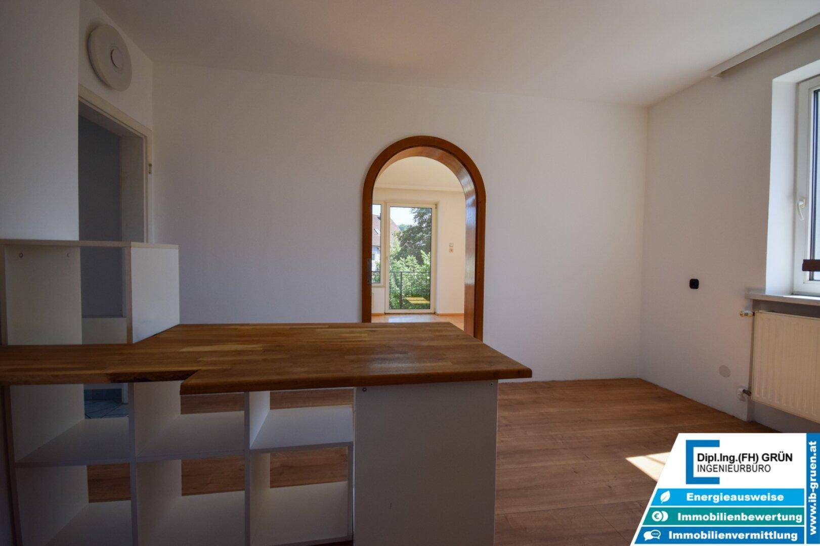 Heller Wohn- und Essbereich mit Holzboden und einem Rundbogen, der zum Balkon führt.