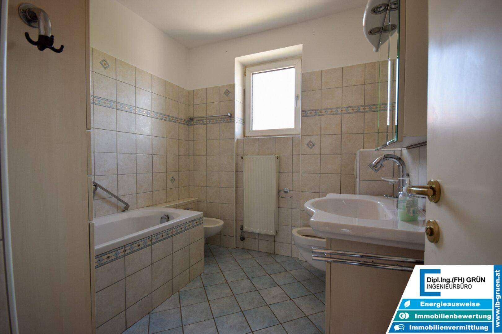 Gefliestes Badezimmer mit Badewanne, Waschbecken, Toilette und Fenster für natürliche Belüftung.