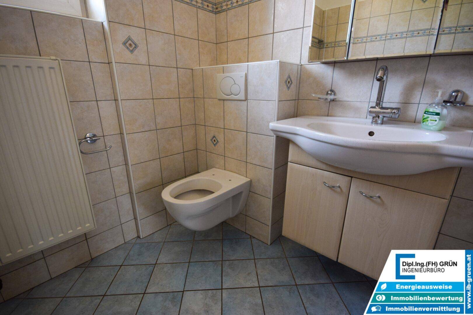 Gefliestes Badezimmer mit wandhängender Toilette und Waschbecken mit Unterschrank.