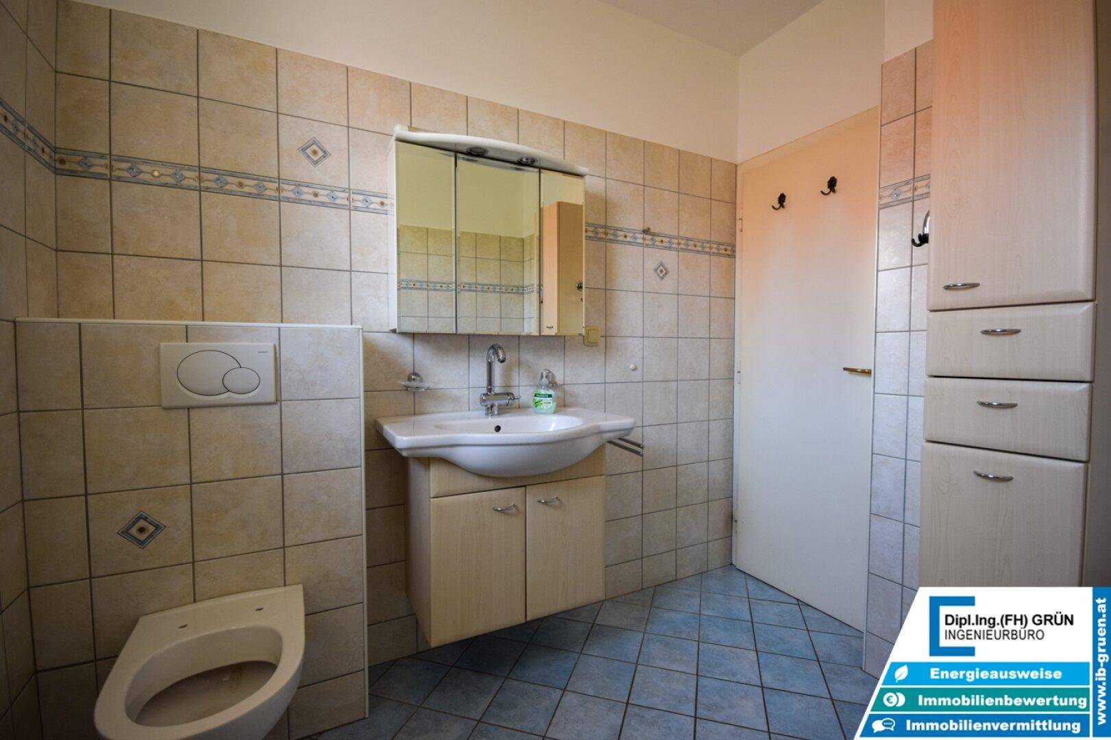 Gefliestes Badezimmer mit Waschbecken, Toilette und Spiegelschrank, in hellem Design.