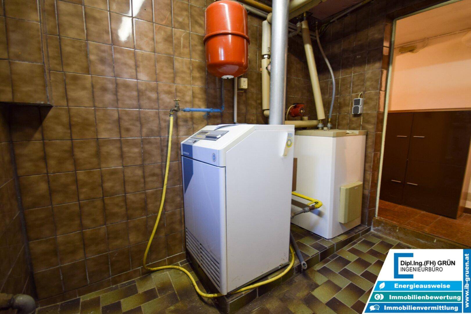 Detailansicht des Heizkessels und der Installationen in einem gefliesten Kellerraum.