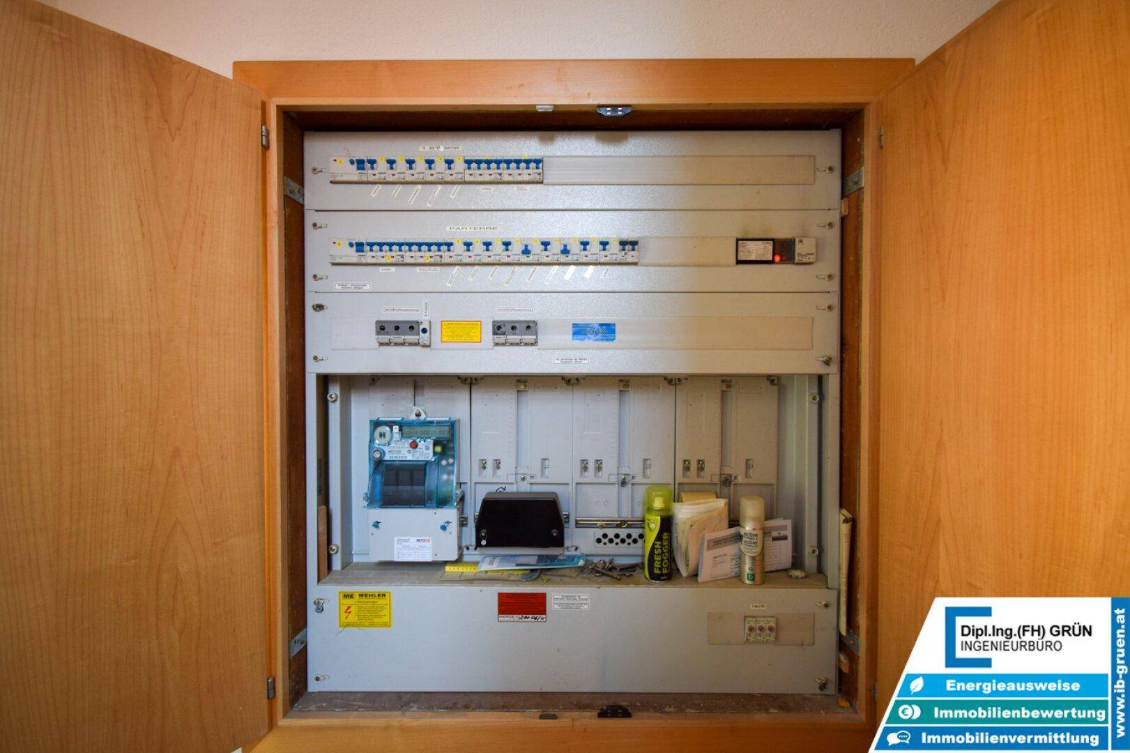 Offener Sicherungskasten in einem Holzschrank, zeigt elektrische Installationen.