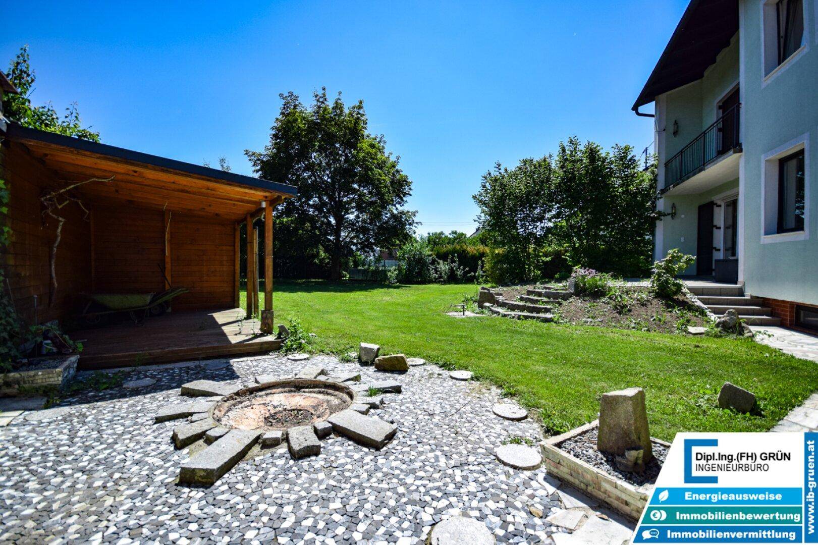 Großer Garten mit Feuerstelle, Holzpergola und weitläufiger Rasenfläche.