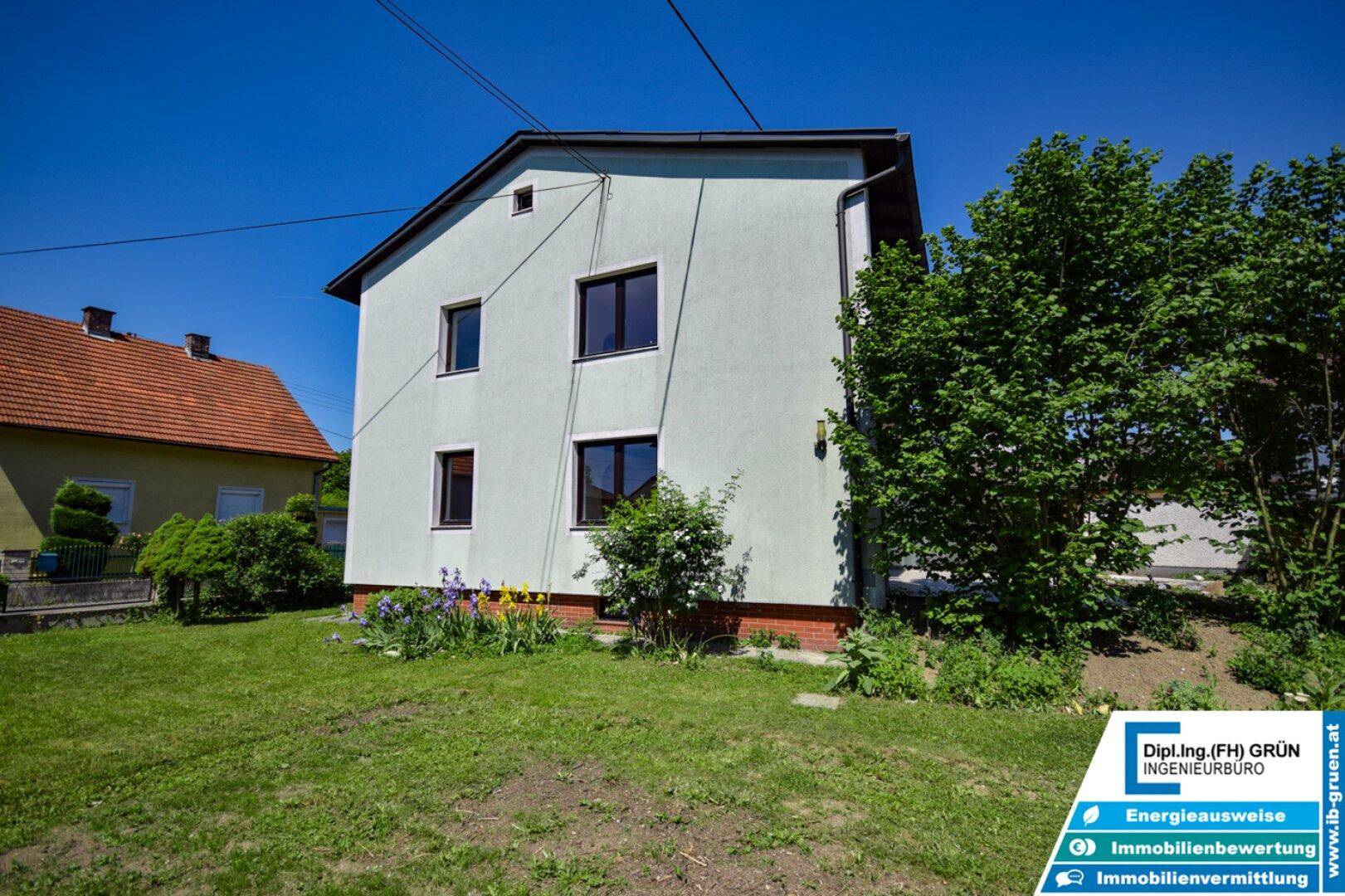 Seitenansicht des Hauses mit Rasenfläche und blühenden Pflanzen im Vorgarten.