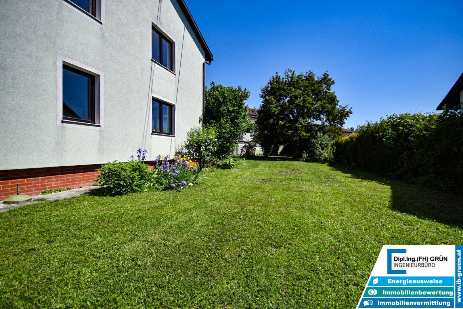 Seitenansicht des Hauses mit langem Rasenstreifen und grünen Büschen.