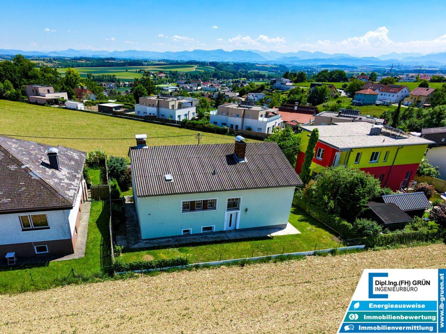 Weitläufige Luftaufnahme des Hauses mit umliegenden Feldern und Bergen im Hintergrund.