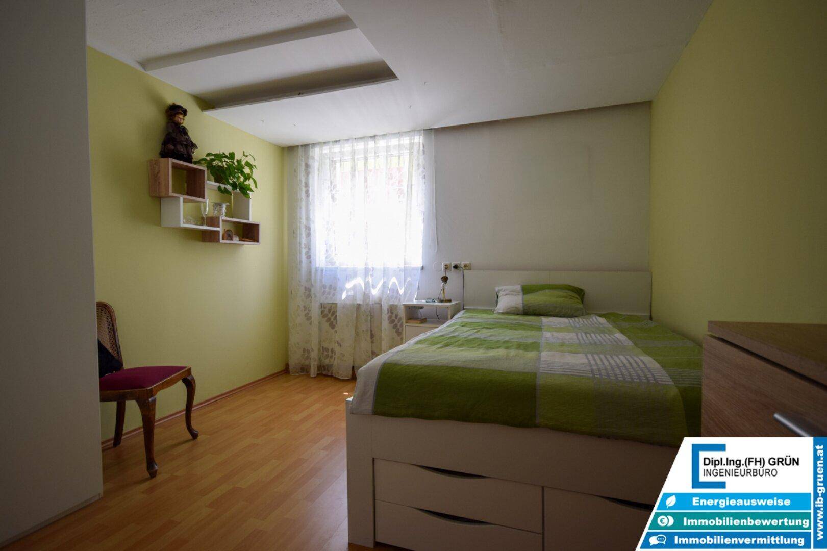 Helles Schlafzimmer mit grün gestrichenen Wänden, Holzboden und einem Bett mit Stauraum.