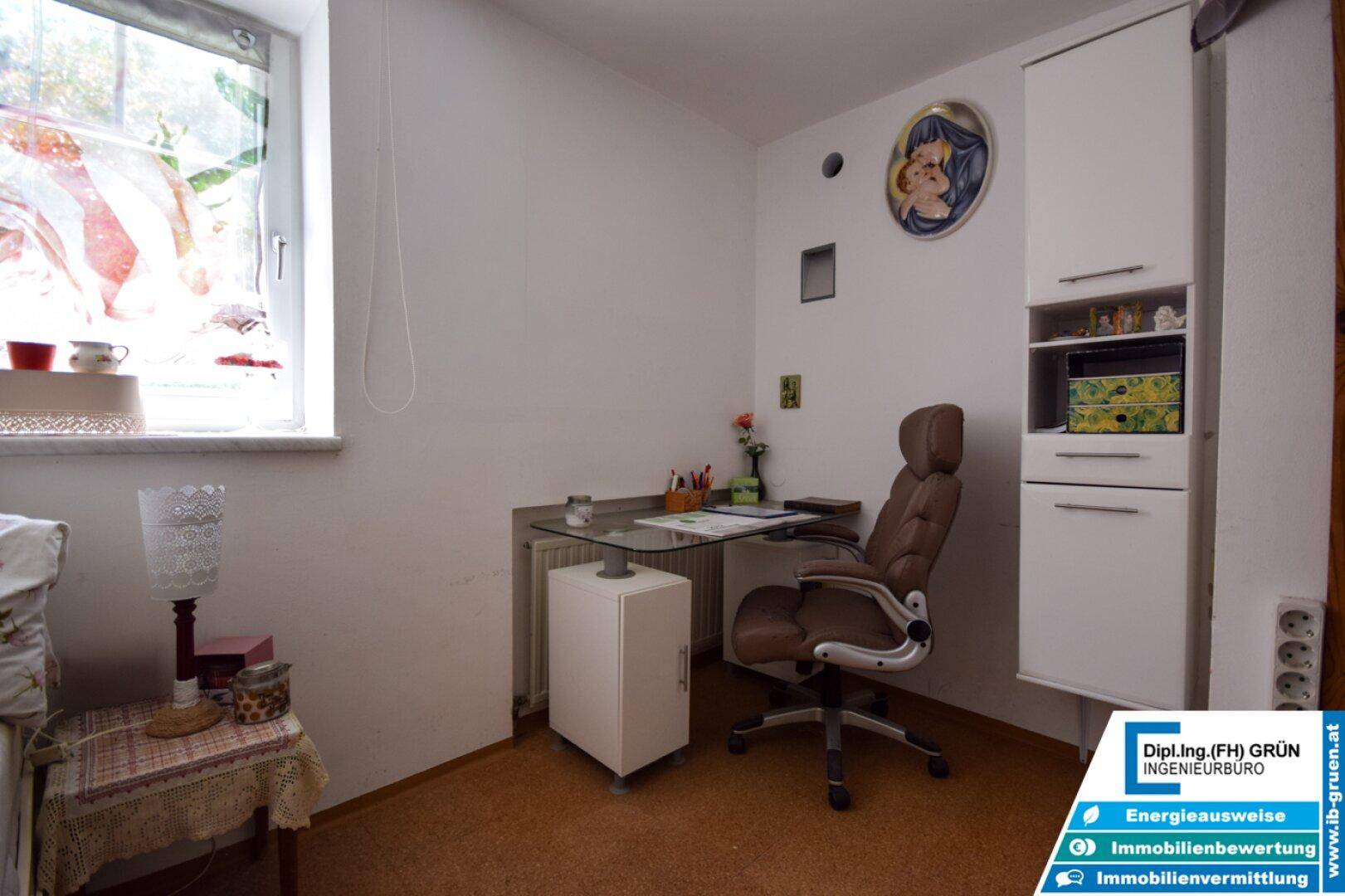 Arbeitsbereich in einem Zimmer mit Schreibtisch, Stuhl und Stauraum unter dem Fenster.