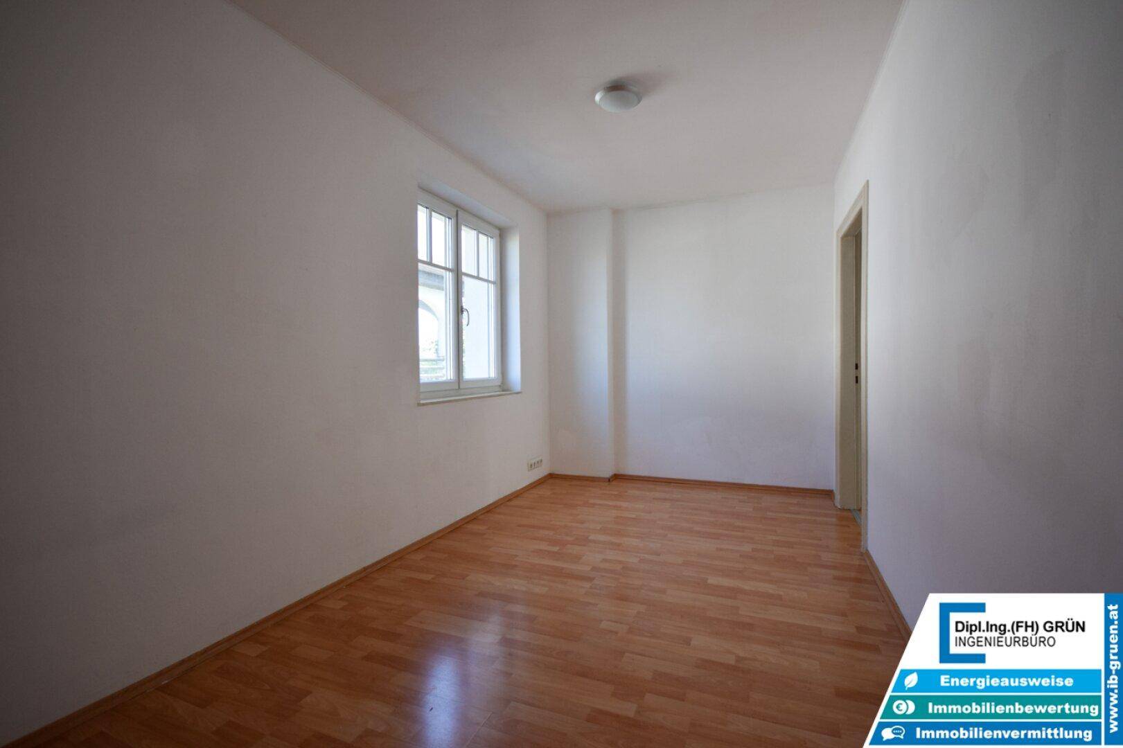 Freundliches Zimmer mit Laminatboden und weiß gestrichenen Wänden, bereit zur individuellen Gestaltung.