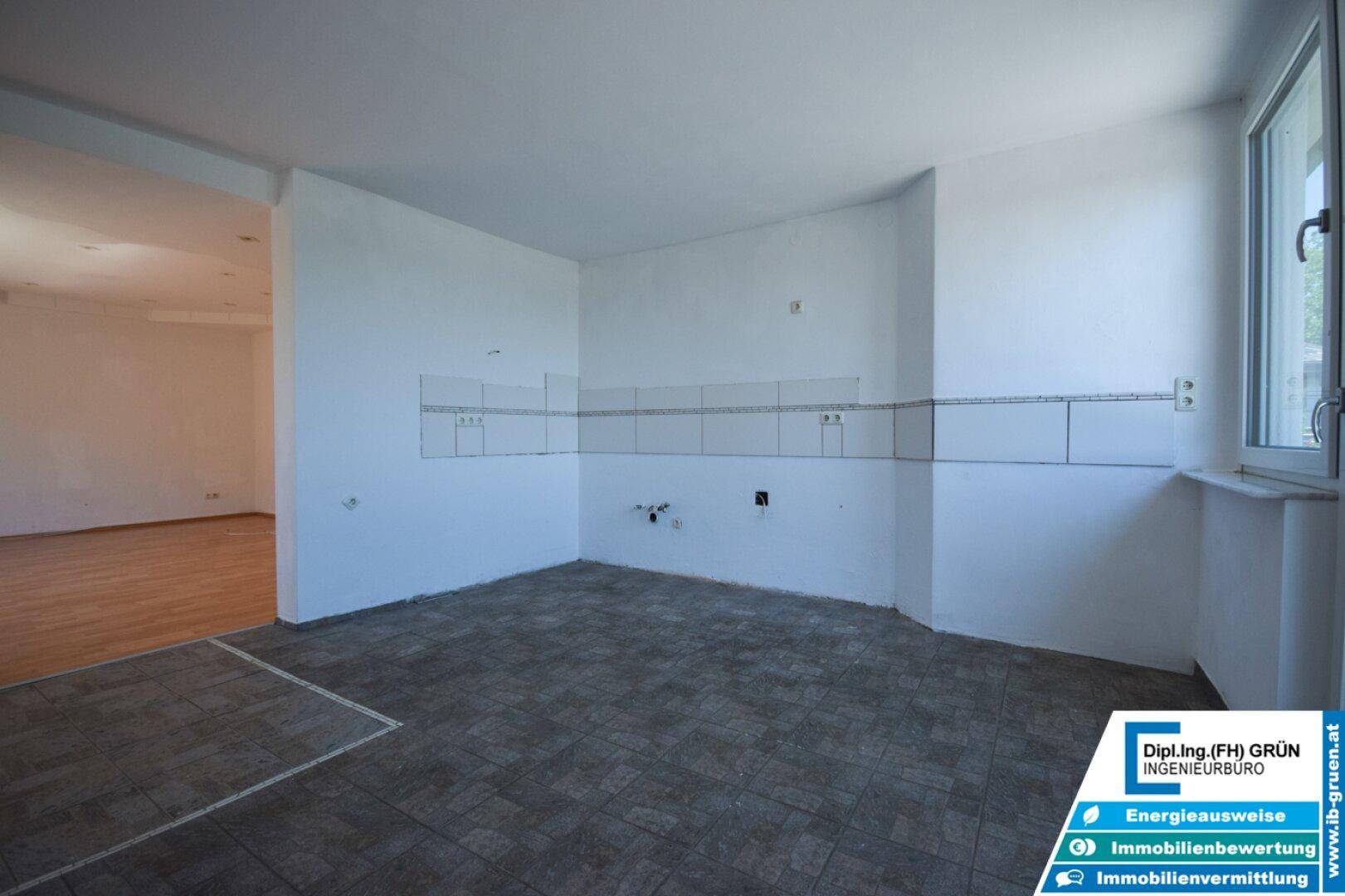 Unmöblierte Küche mit dunklem Fliesenboden und Fliesenspiegel, offen zum angrenzenden Wohnbereich.