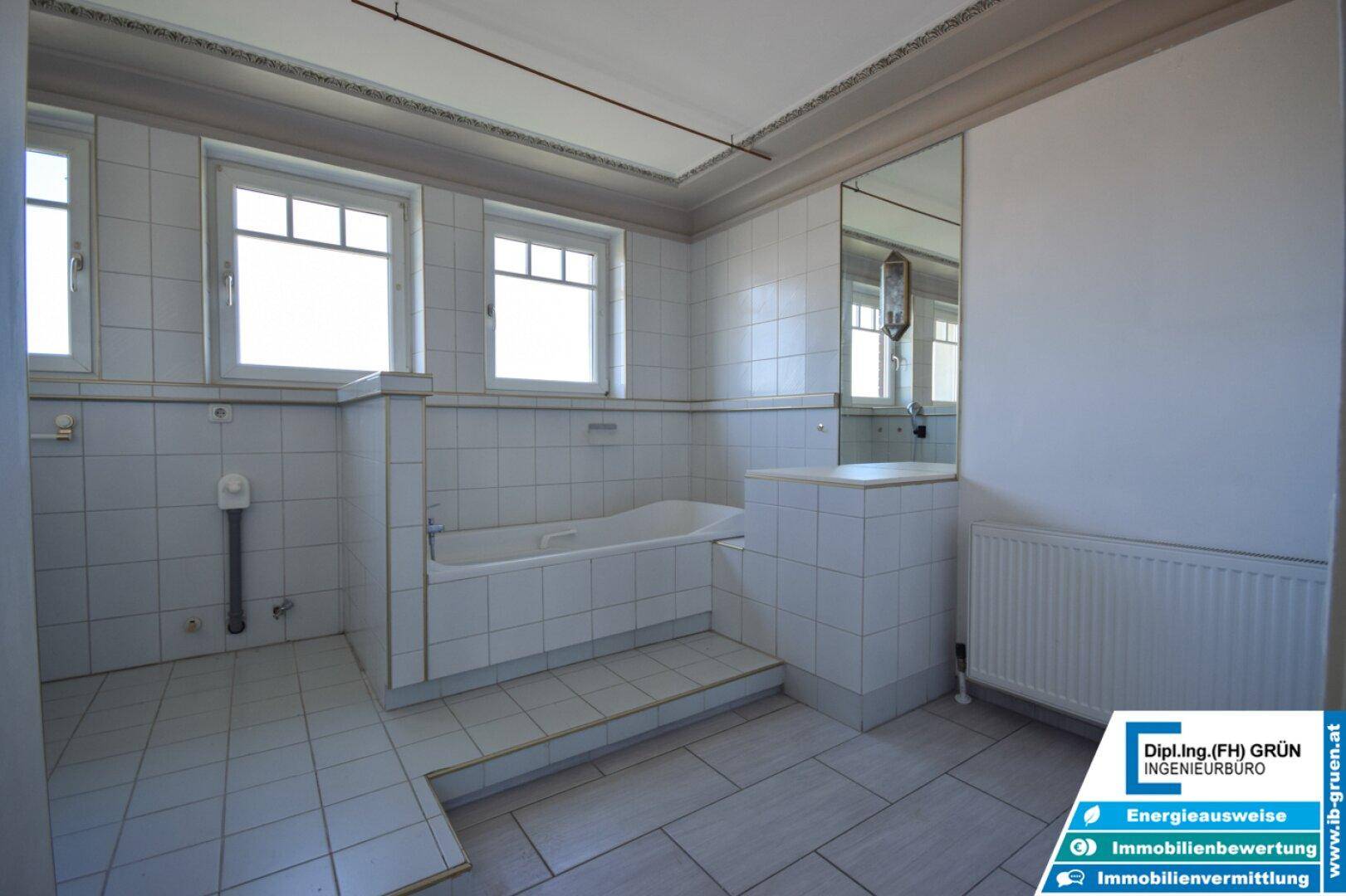 Geräumiges Badezimmer mit Badewanne, weißen Fliesen und zwei Fenstern für Tageslicht.