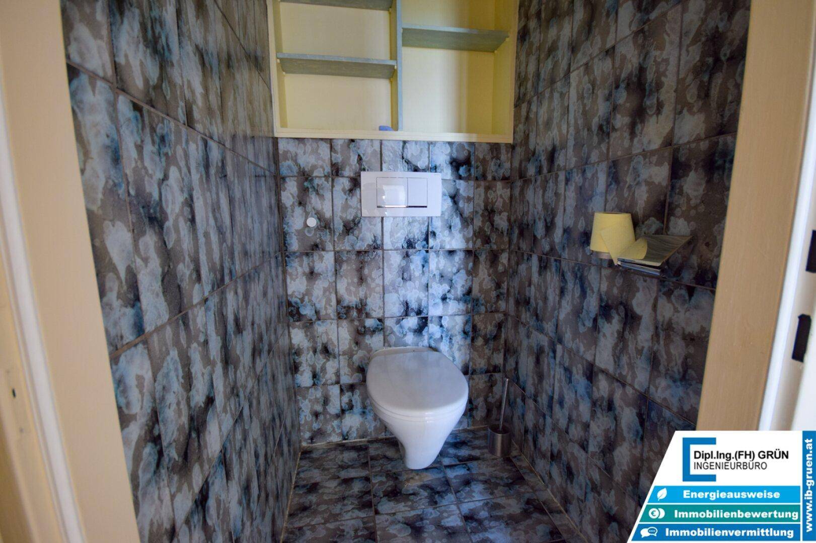 Kleines Gäste-WC mit dunklen, gemusterten Fliesen und Wand-WC.