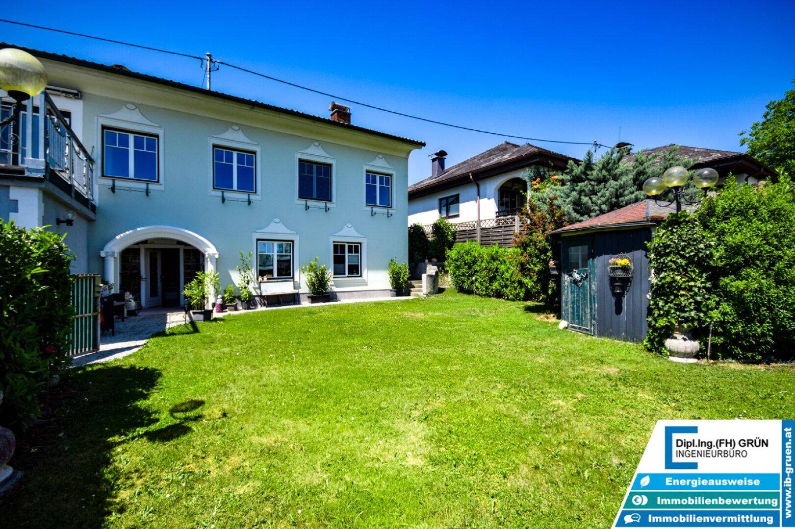 Gepflegter Garten mit Rasenfläche, Sträuchern und einem Gartenhaus neben dem Wohngebäude.