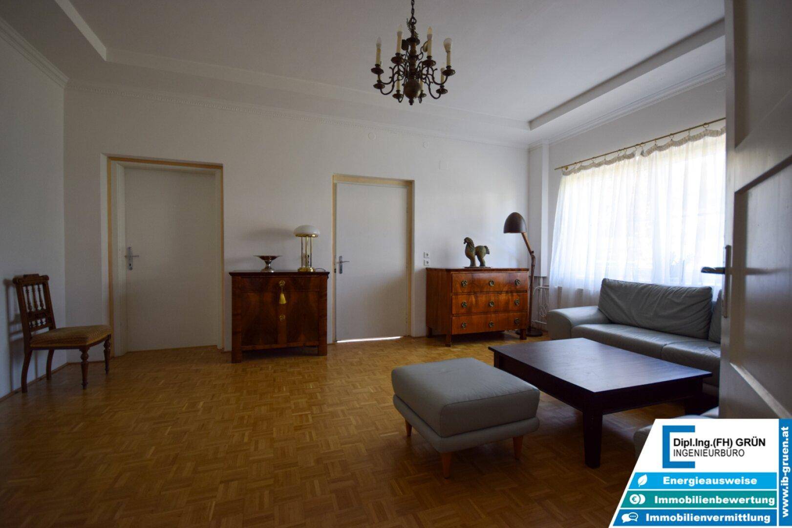 Helles Wohnzimmer mit Parkettboden, klassischem Kronleuchter und bequemer Couch.