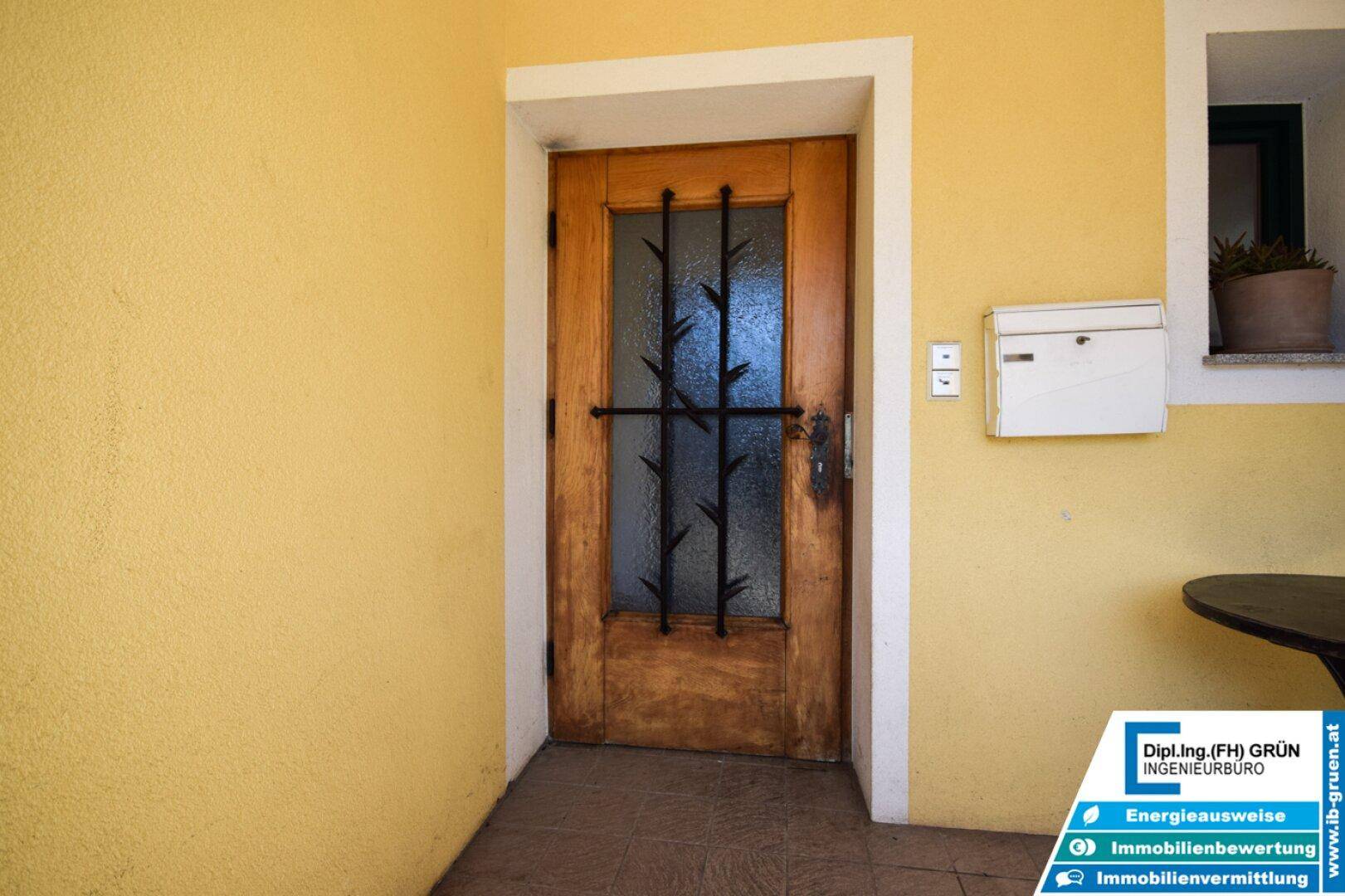Detailansicht der hölzernen Eingangstür mit Glaseinsatz und schmiedeeisernem Gitter.