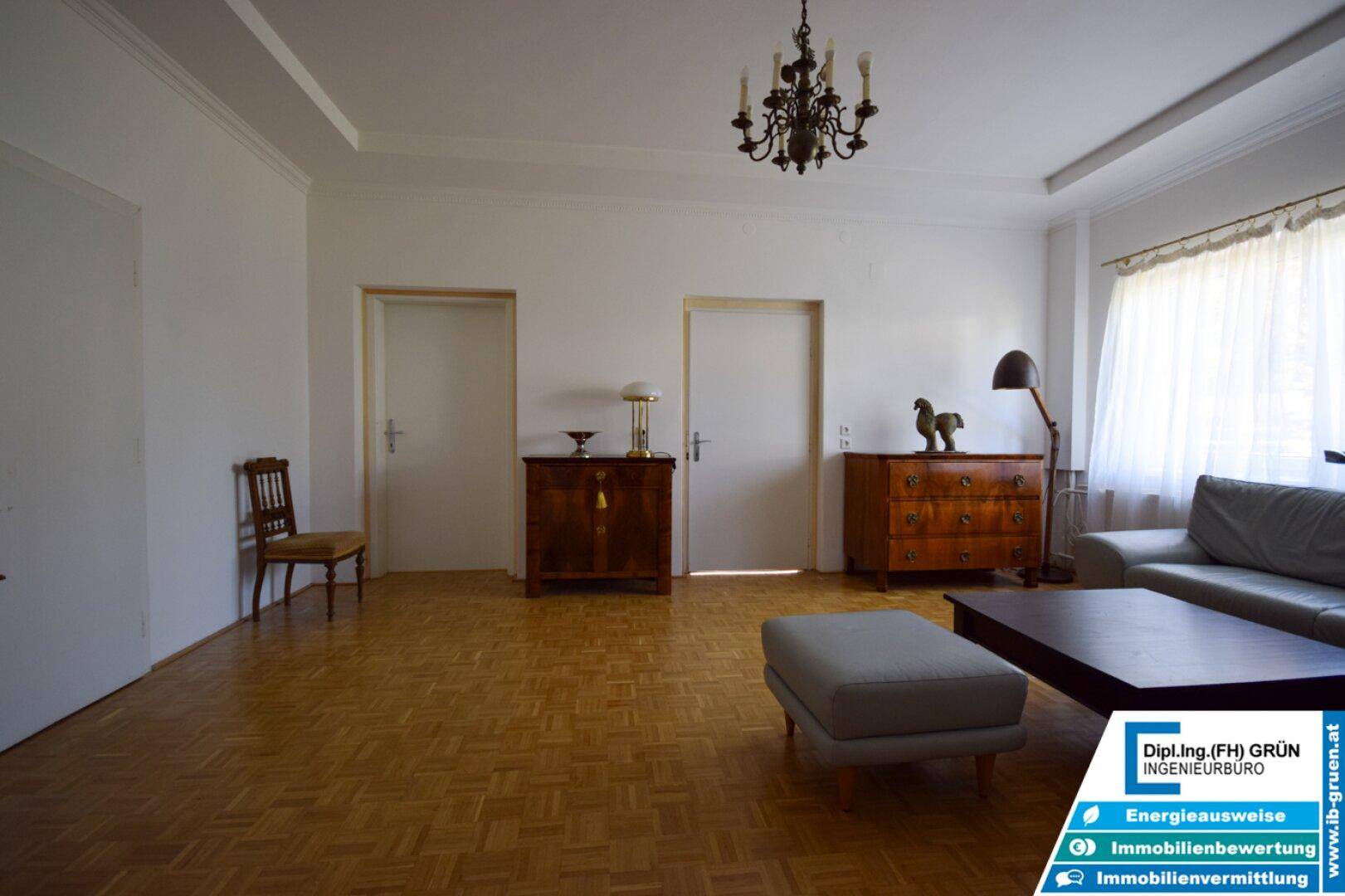 Helles Wohnzimmer mit Parkettboden, klassischem Kronleuchter und bequemer Couch.