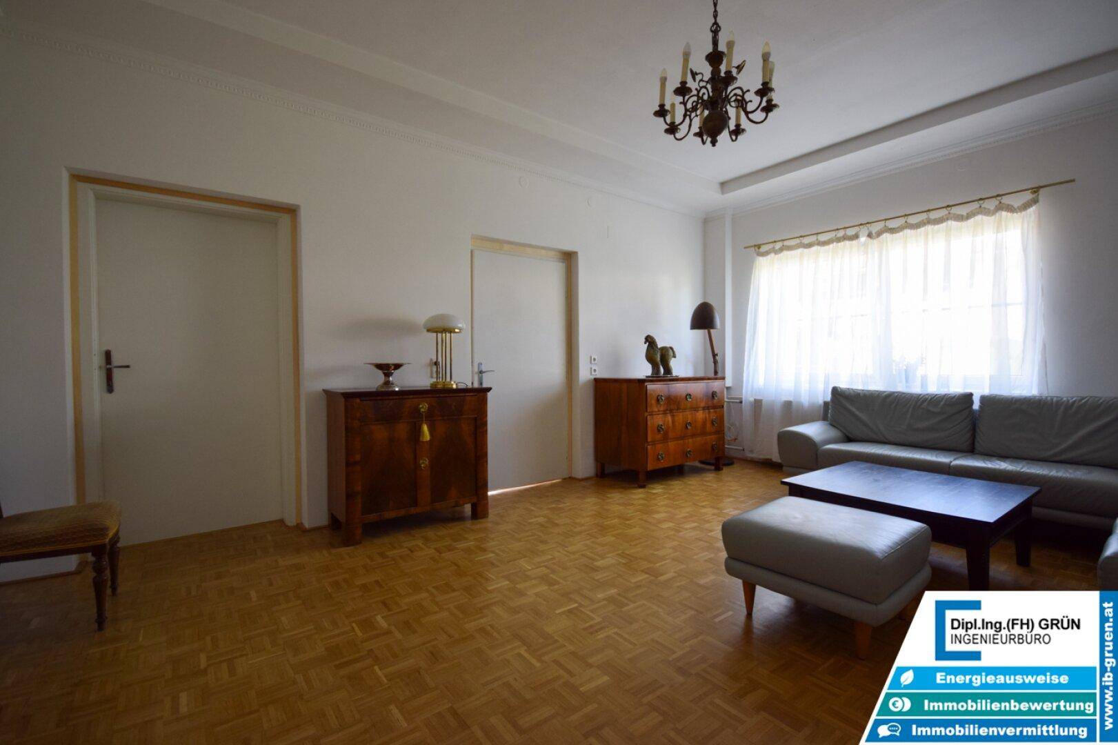 Helles Wohnzimmer mit Parkettboden, klassischem Kronleuchter und bequemer Couch.