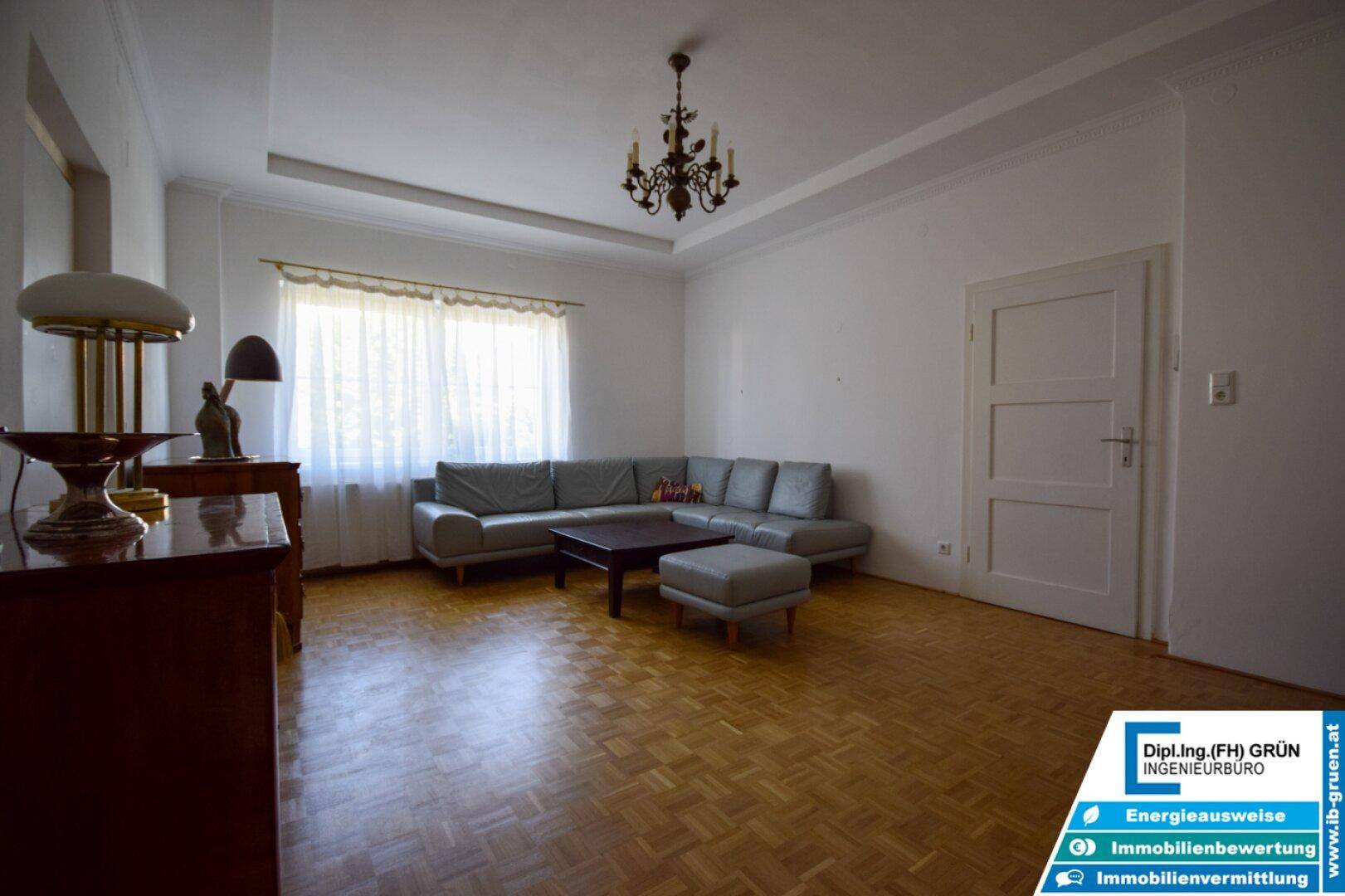 Geräumiges Wohnzimmer mit Parkettboden, großem Fenster und gemütlicher Sitzecke.
