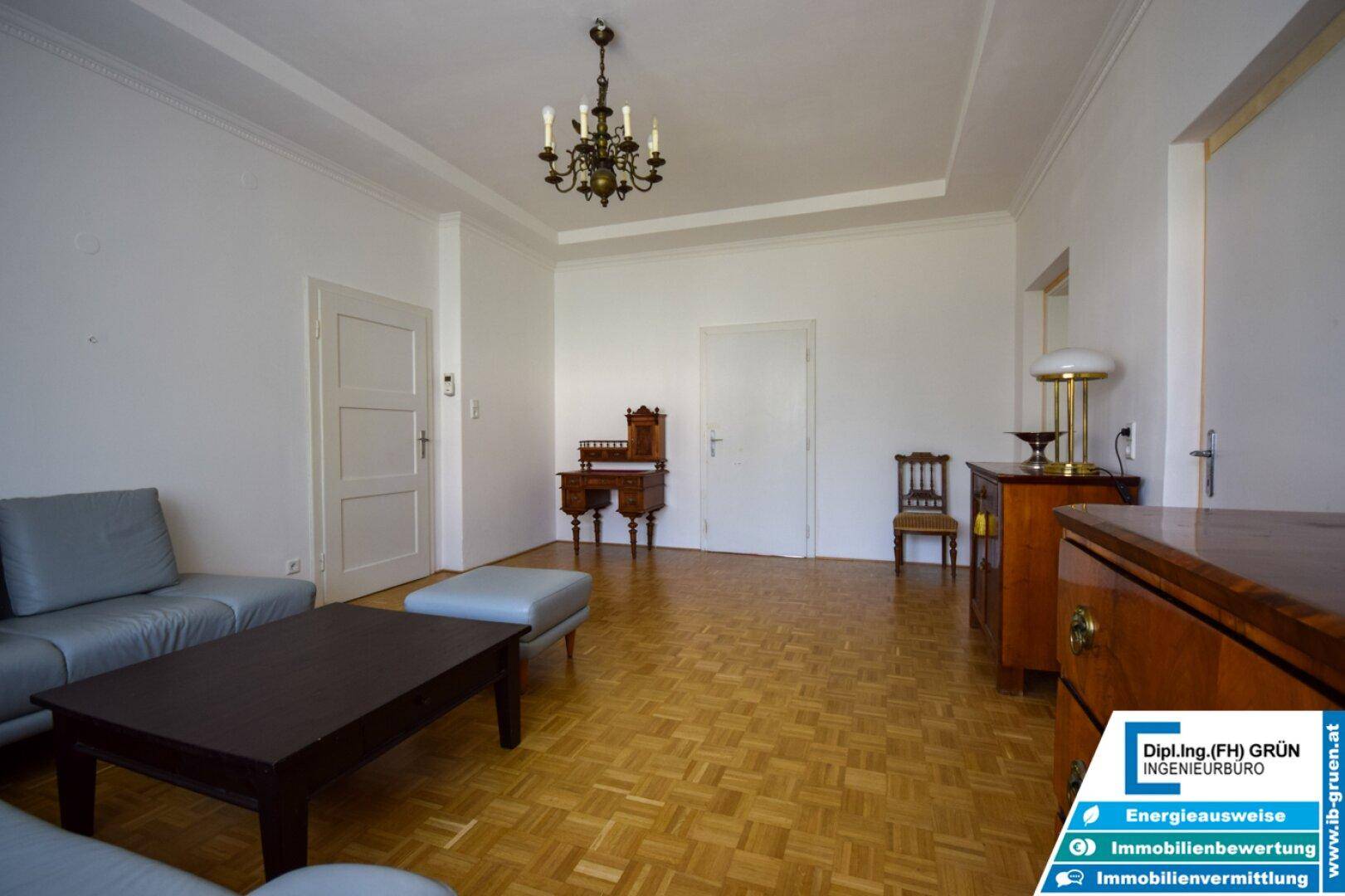 Wohnzimmer mit Parkettboden, Couch und antiken Möbeln unter einem Kronleuchter.