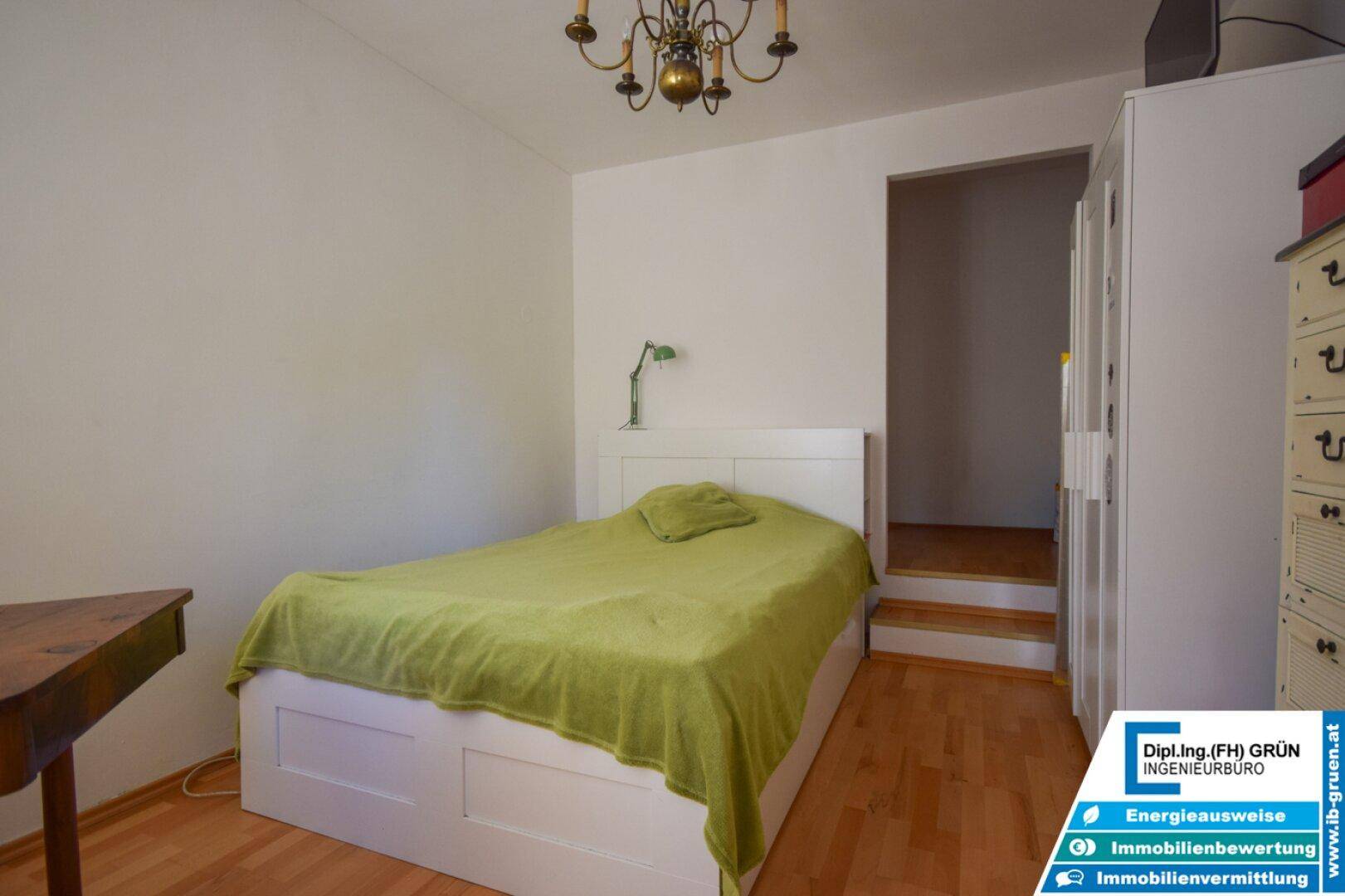 Schlafzimmer mit Einzelbett, Parkettboden und Zugang zu einem angrenzenden Raum.
