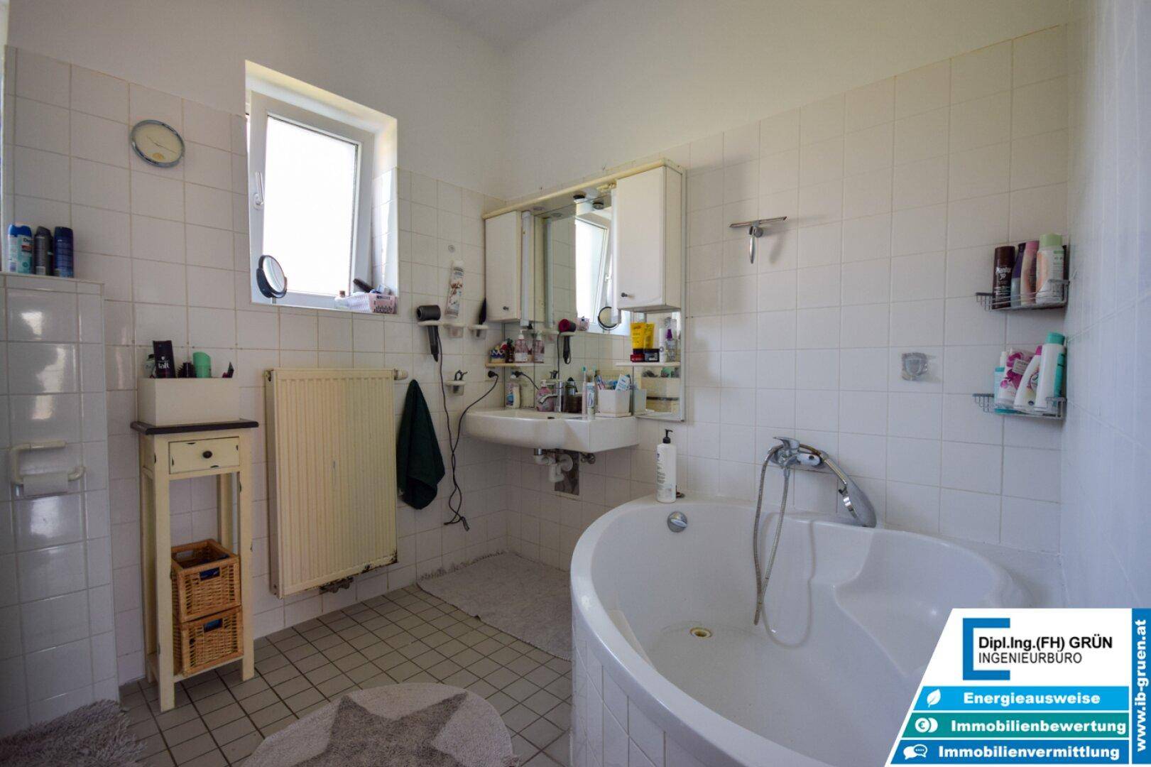 Badezimmer mit Badewanne, Waschbecken, Spiegelschrank und Fenster für Tageslicht.