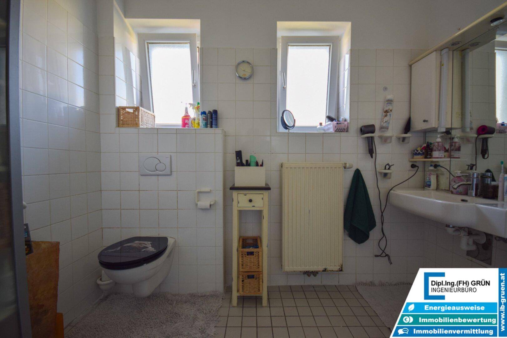 Badezimmer mit WC, Waschbecken, Spiegelschrank und zwei Fenstern für gute Belüftung.
