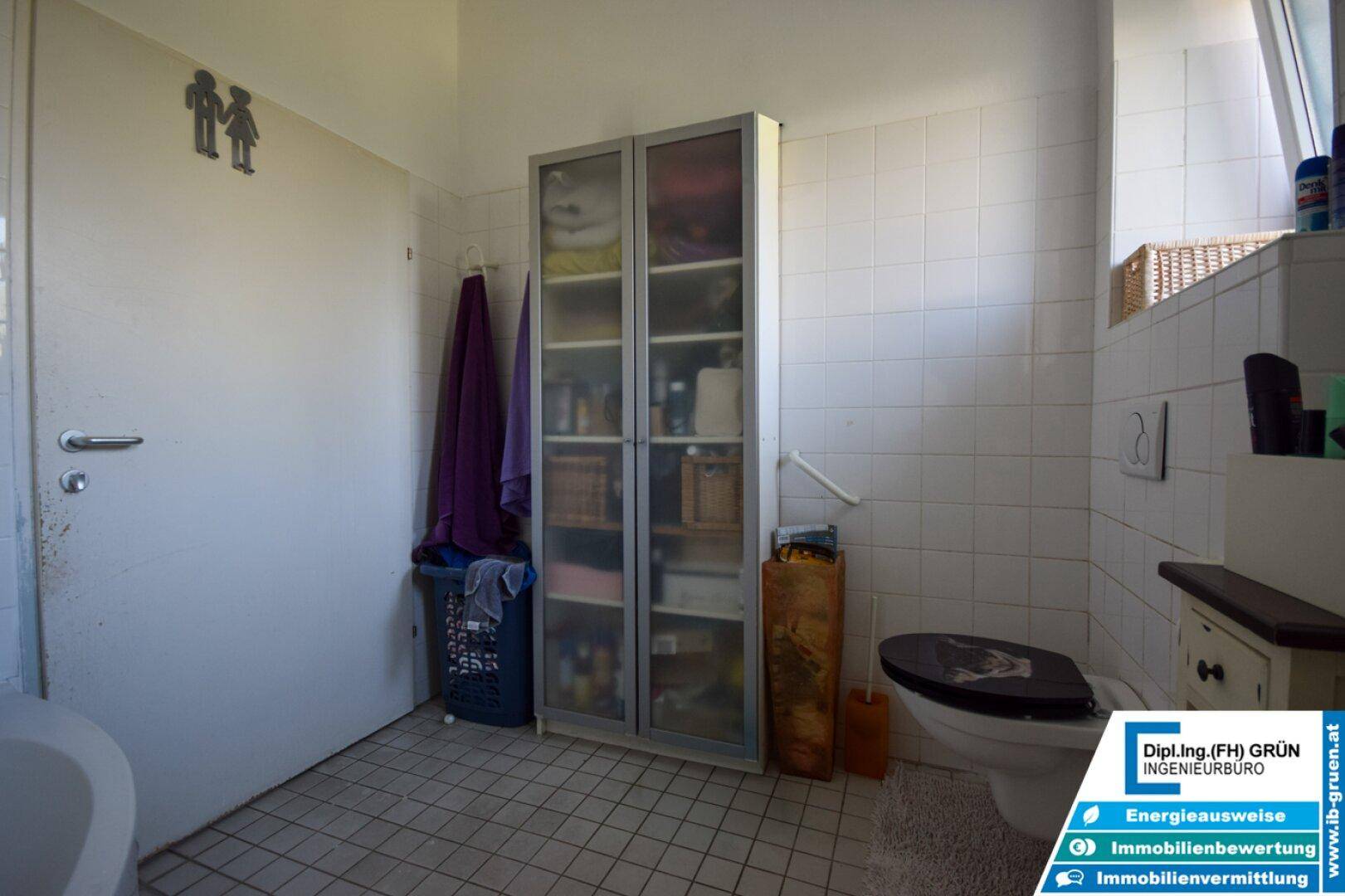 Badezimmer mit WC, Badewanne und einem praktischen Glasschrank für Handtücher und Utensilien.