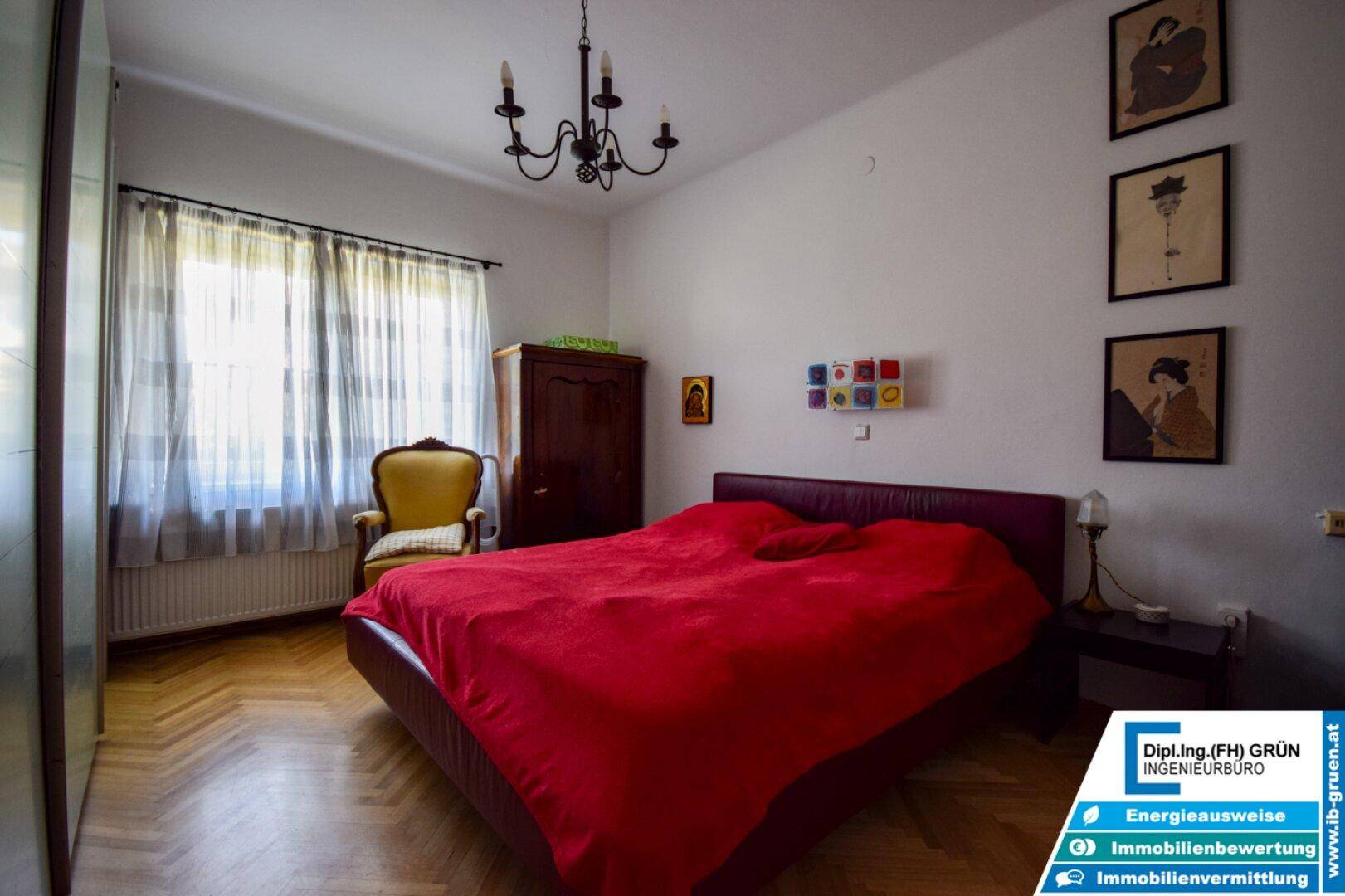 Schlafzimmer mit Doppelbett, Parkettboden, Kleiderschrank und einem eleganten Kronleuchter.