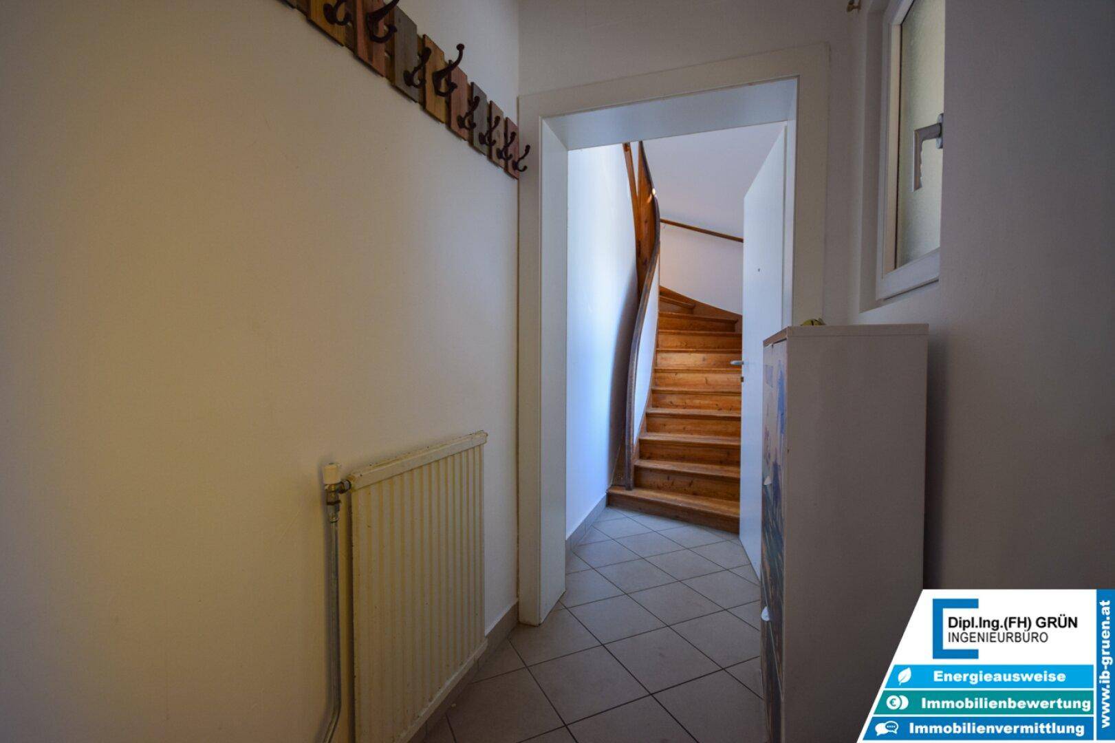 Flur mit Fliesenboden, Heizkörper und einer Holztreppe, die zum Obergeschoss führt.