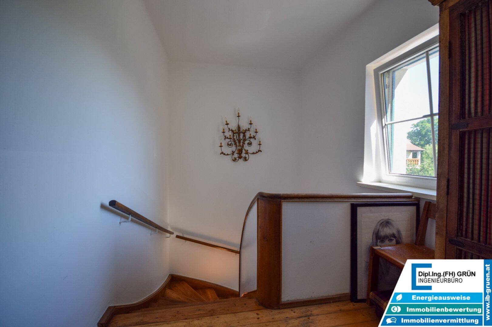 Treppenhaus mit Holztreppe, Fenster und einem dekorativen Kronleuchter an der Wand.