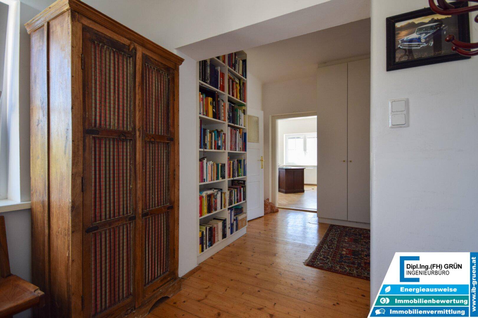 Flur mit Holzboden, Bücherregal und einem antiken Schrank, der viel Stauraum bietet.