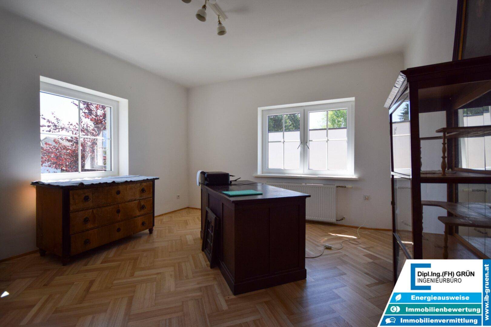 Helles Büro mit Parkettboden, zwei großen Fenstern und antiken Möbeln.