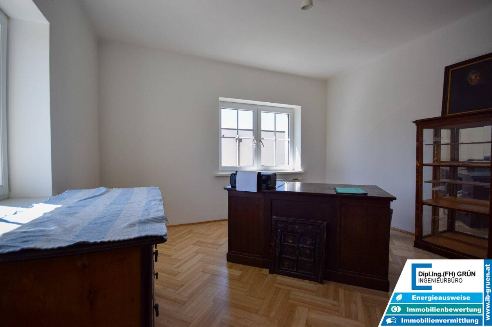 Büro mit Parkettboden, Schreibtisch und Fenster, das den Raum gut beleuchtet.
