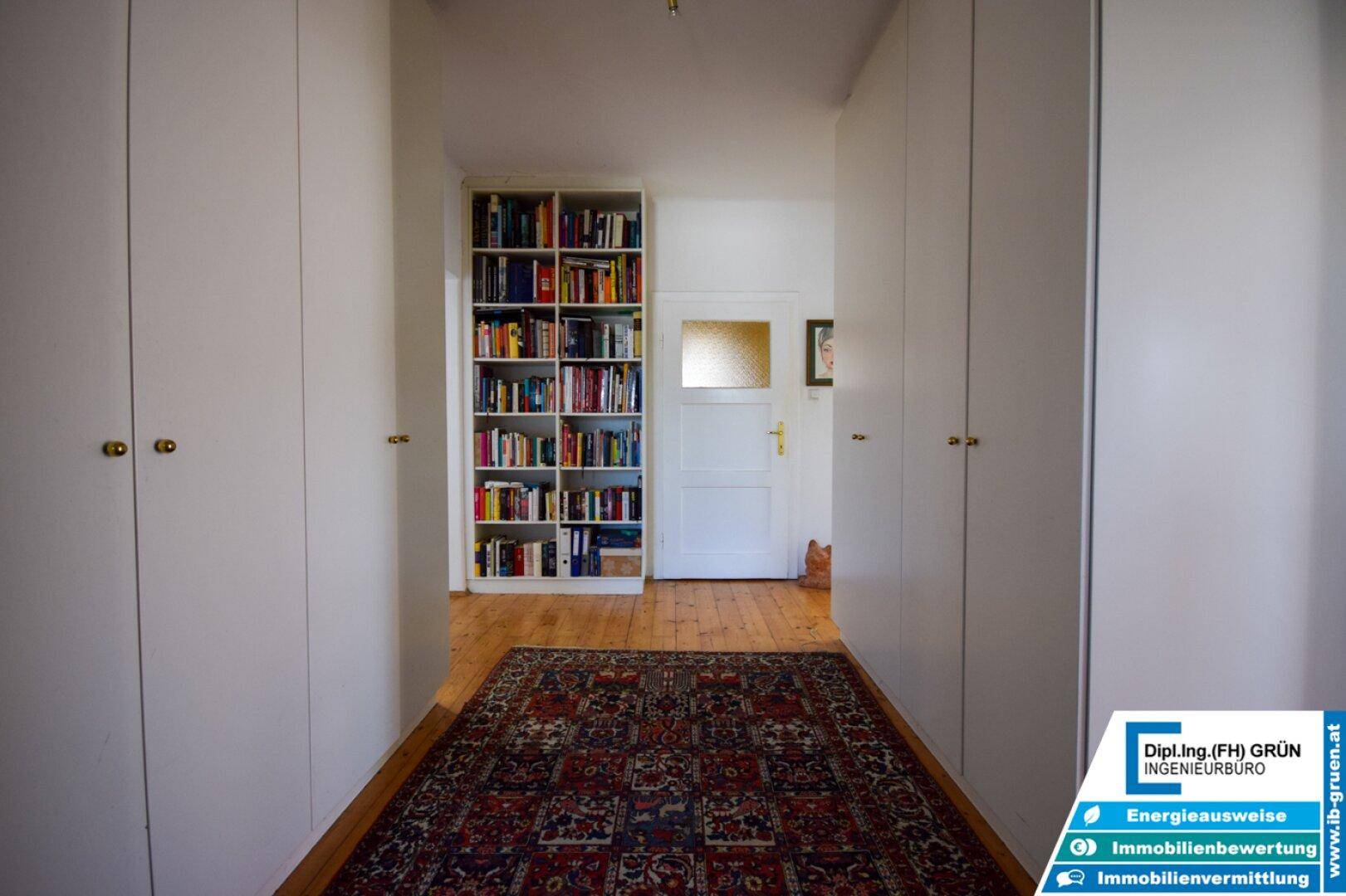 Langer Flur mit Holzboden, Einbauschränken und einem Bücherregal für zusätzlichen Stauraum.
