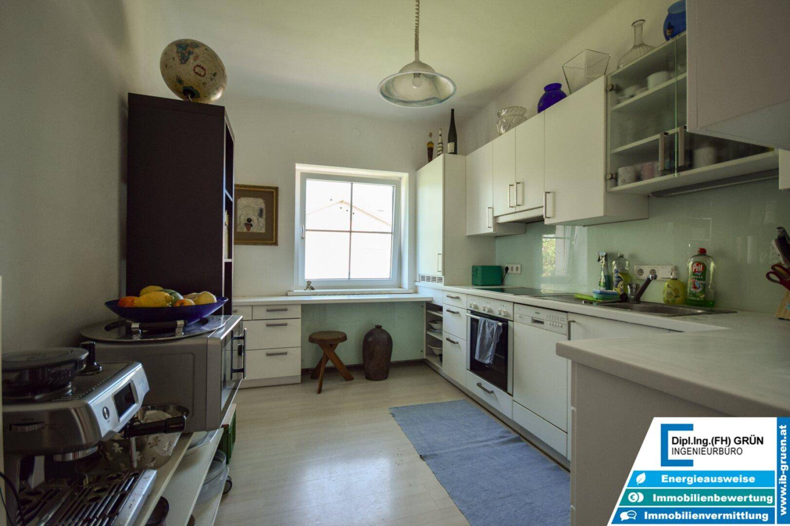 Helle Küche mit weißen Schränken, Fenster und modernen Geräten, ideal zum Kochen.