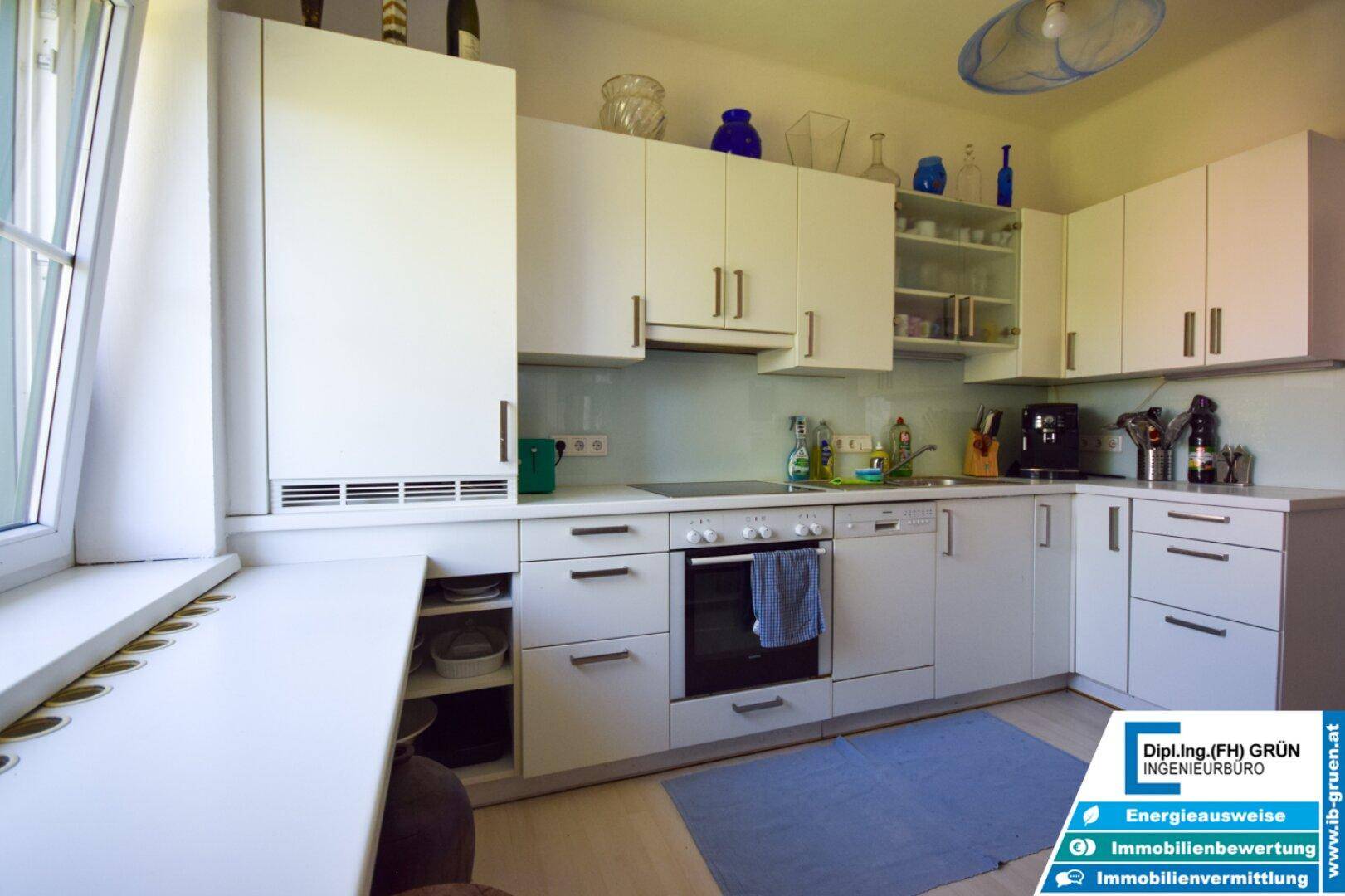 Moderne Küche mit weißen Schränken, Induktionskochfeld, Backofen und Fenster.