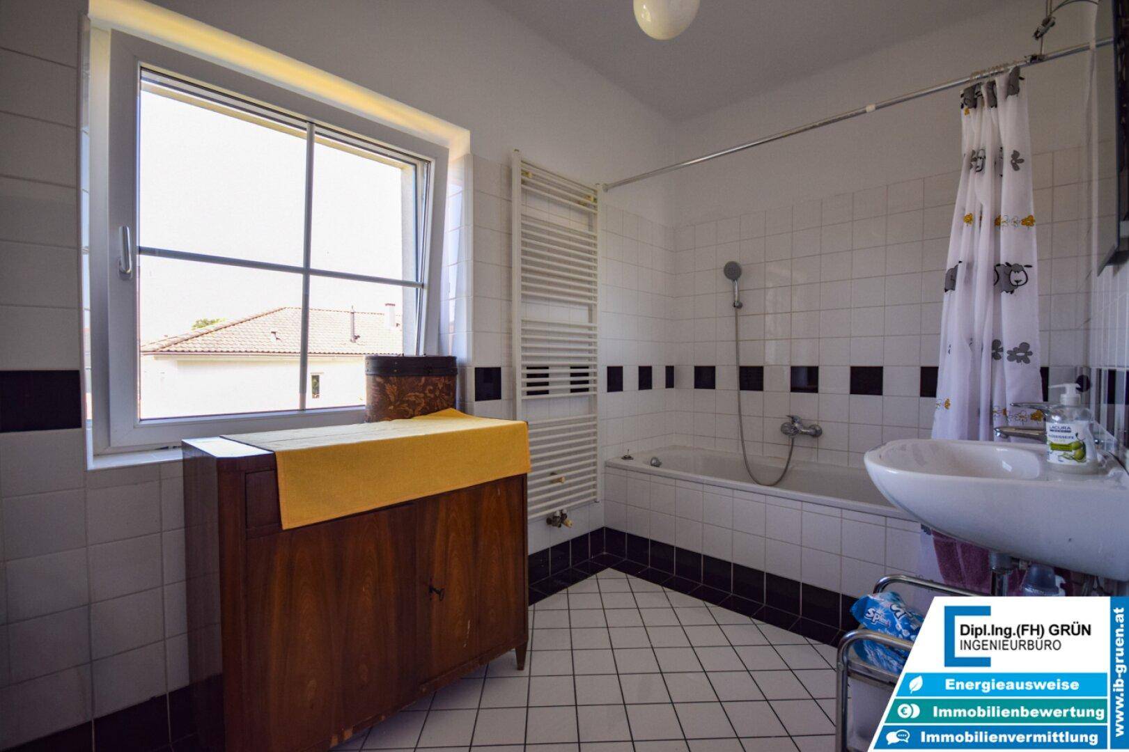 Badezimmer mit Badewanne, Waschbecken, beheiztem Handtuchhalter und Fenster.